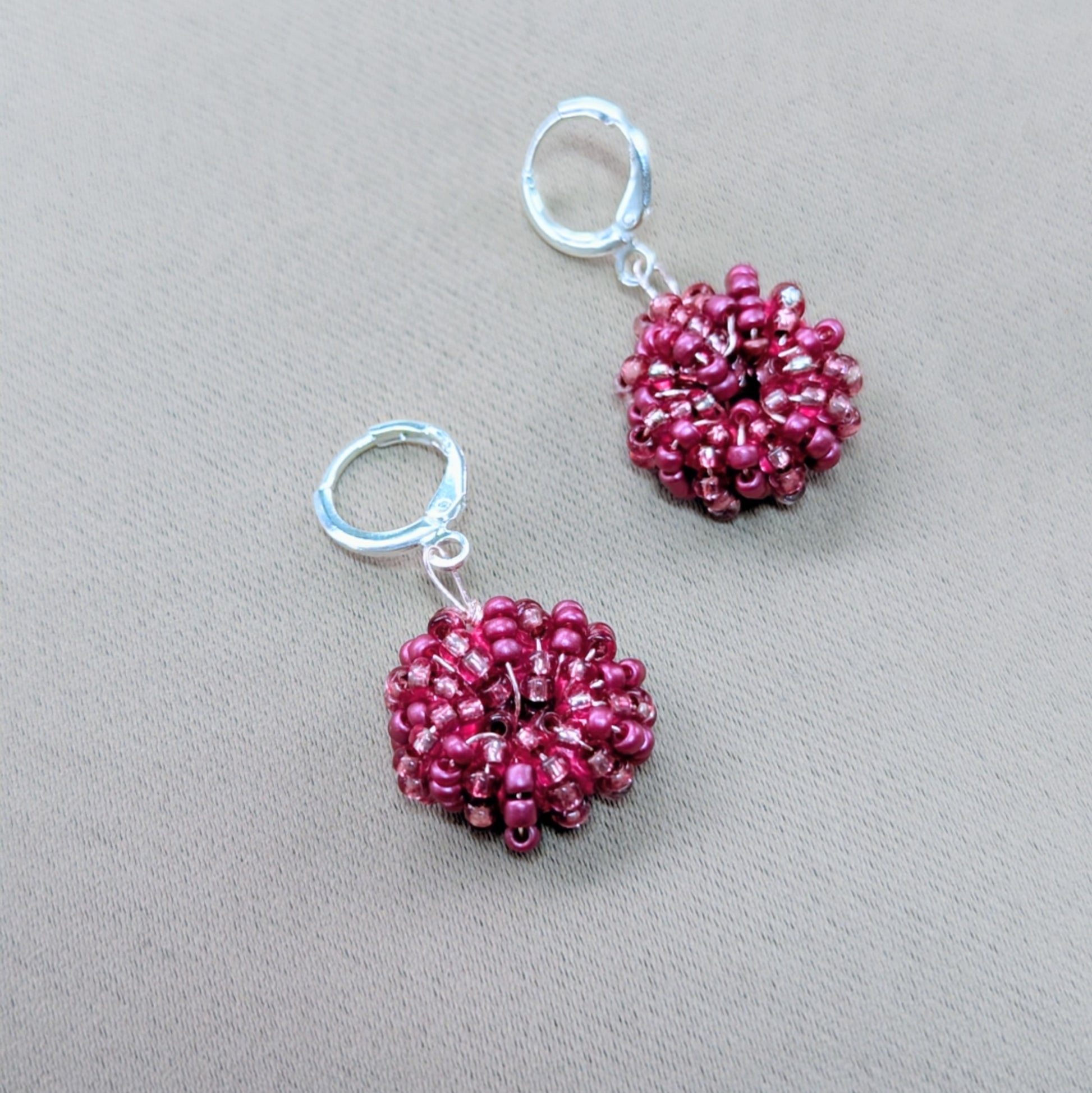 Small round pink handmade earrings held between fingers, glowing softly in natural light.
