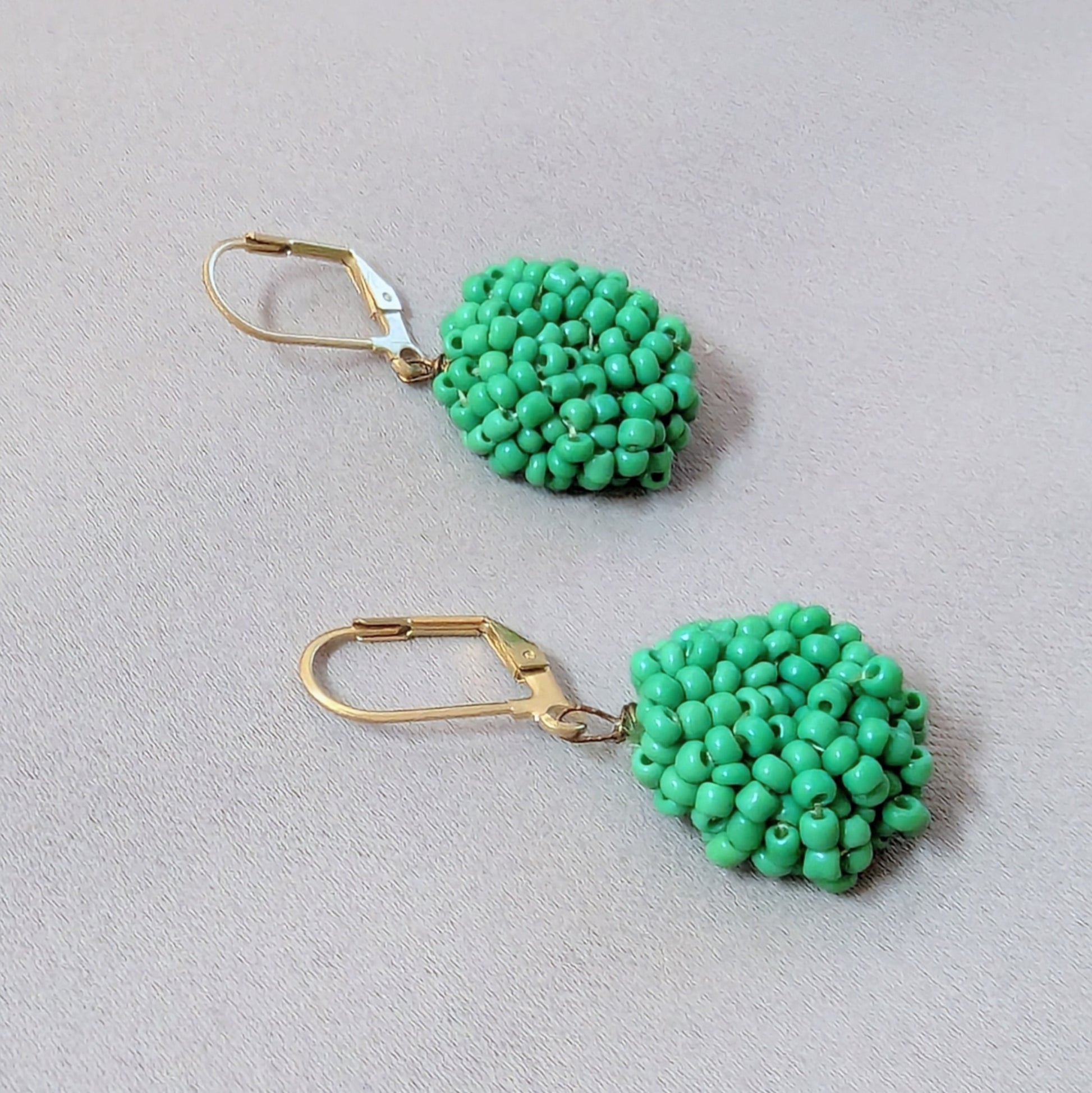 Side angle of green and gold handmade earrings showing fine bead weaving and durable construction.