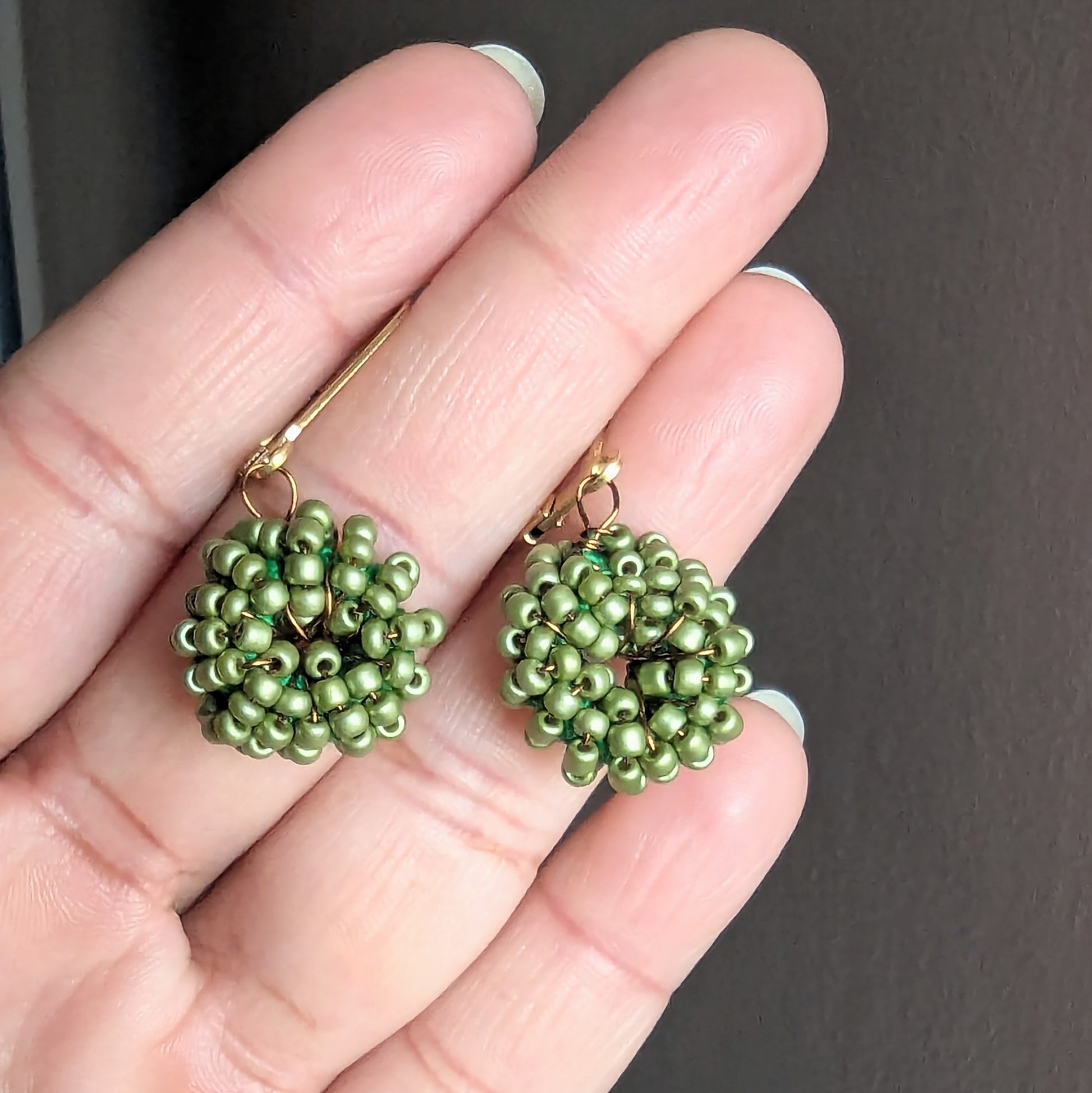 Close-up of artisan-made green beaded earrings with gold stainless steel clasps.