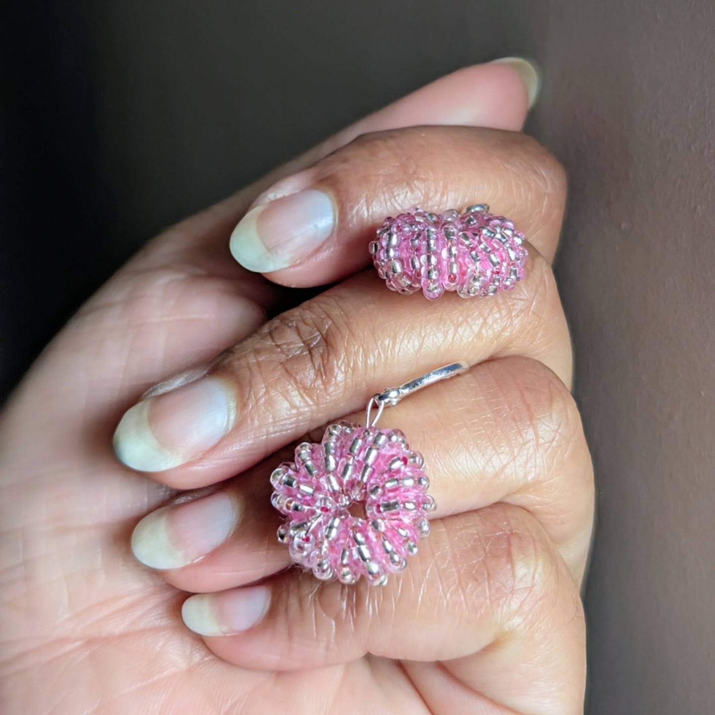 Pair of radiant pink seed bead earrings held in hand, handcrafted by Indian artisan Megha.