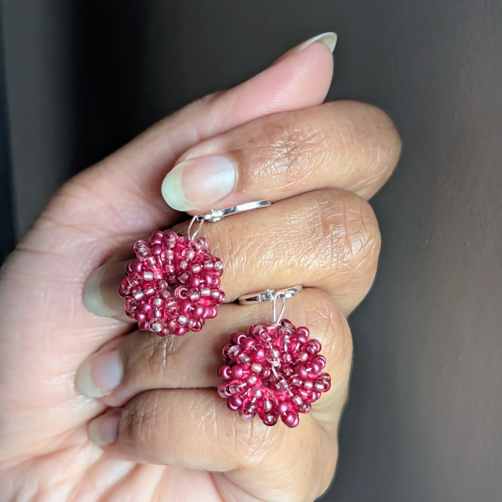 Vibrant berry pink artisan earrings crafted from glass seed beads and rose gold wire, resting gently on hand.