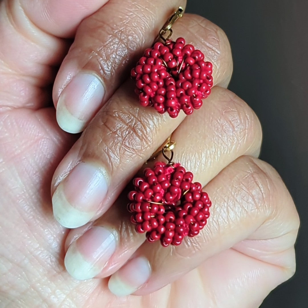 Hand holding one-of-a-kind red hoop style earrings featuring rich berry tones and gold clasps.