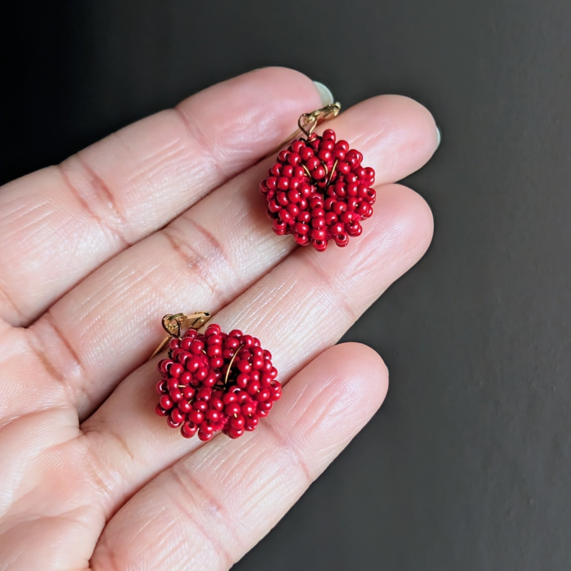 Hand holding a rich red artisan crafted pair of Indian inspired earrings.