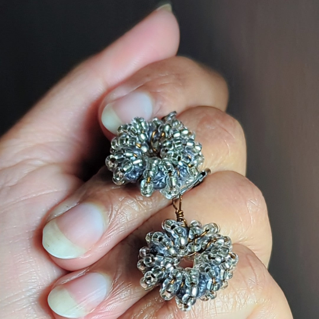 Hand-held silver-grey artisan earrings reflecting natural light.