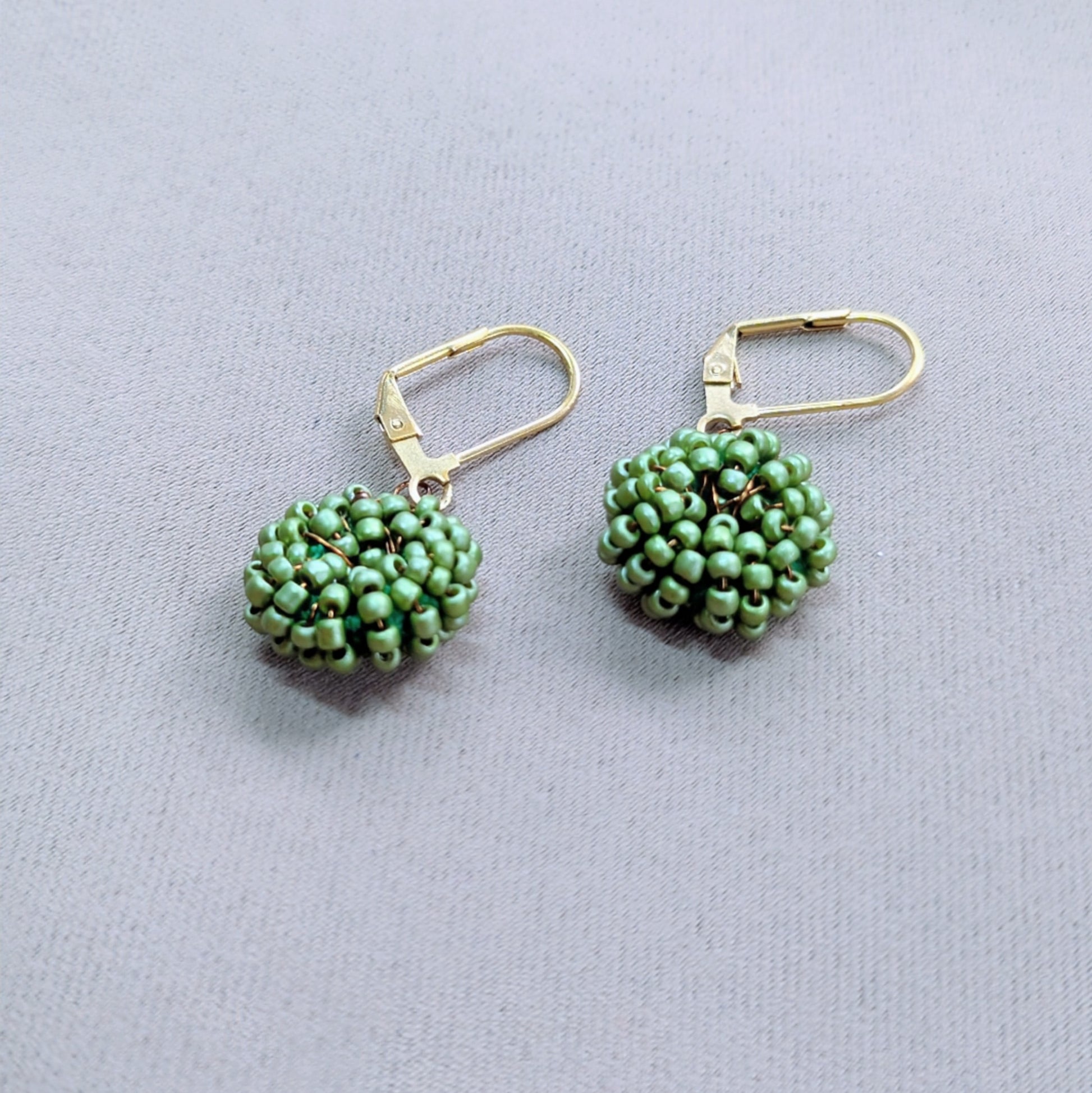 Pair of light green seed bead earrings held in hand, handcrafted by Indian artisan Megha.