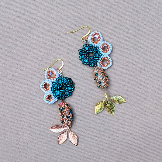 A pair of handmade asymmetric earrings featuring turquoise seahorse motifs, emerald and rose gold scrap beads, and gold plated leaf charms exclusively available at Mayaani Jewellery UK.