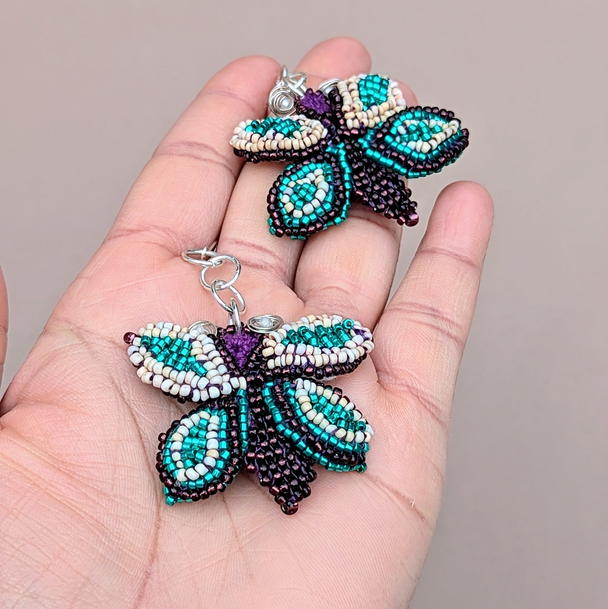 Hand holding a pair of large statement beaded purple, blue and cream butterfly earrings exclusive to Mayaani Jewellery UK.