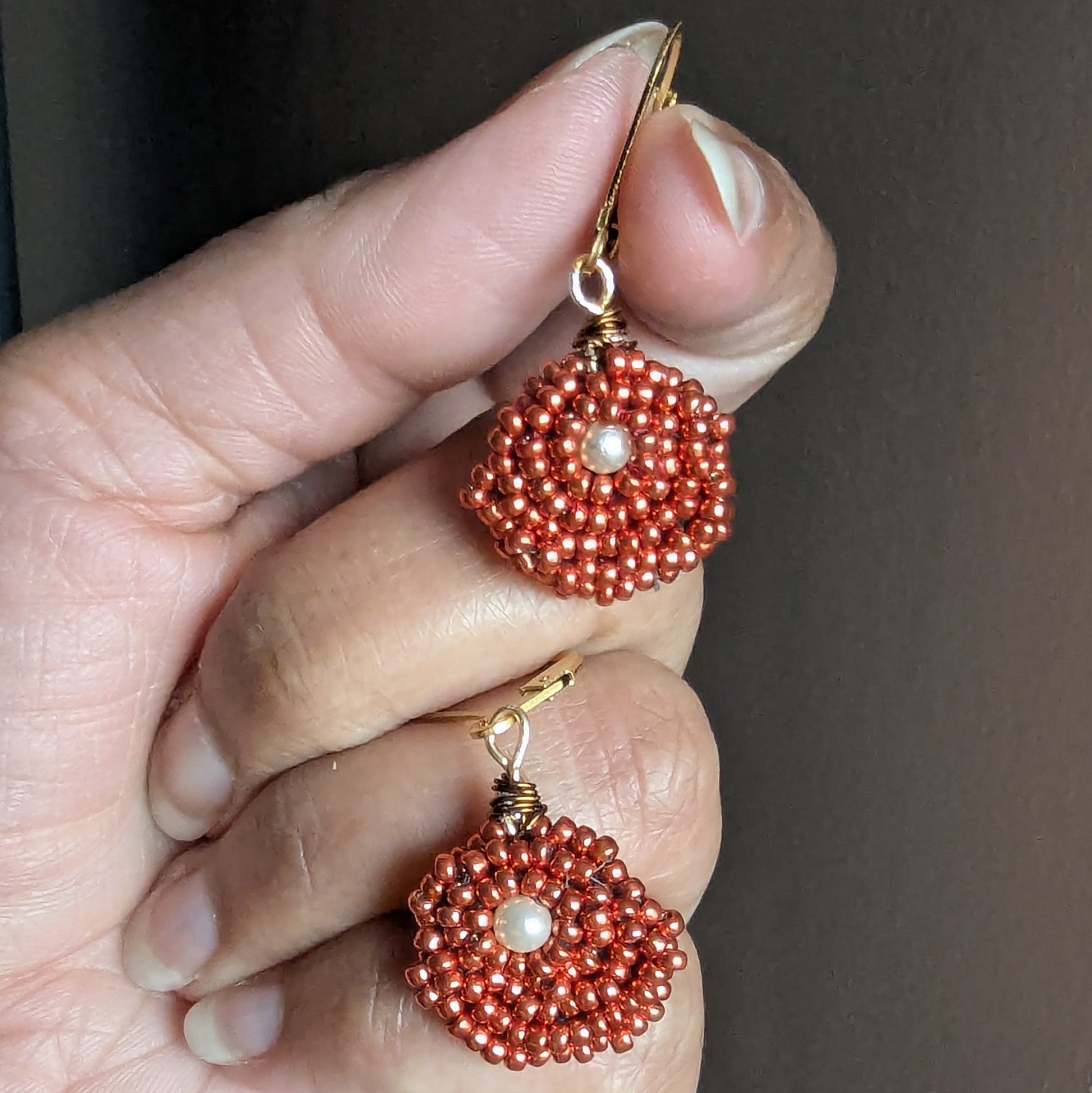 Hand holding an artisan handcrafted pair of designer Indian heritage inspired earrings by Mayaani Jewellery UK featuring copper and pearl accents.