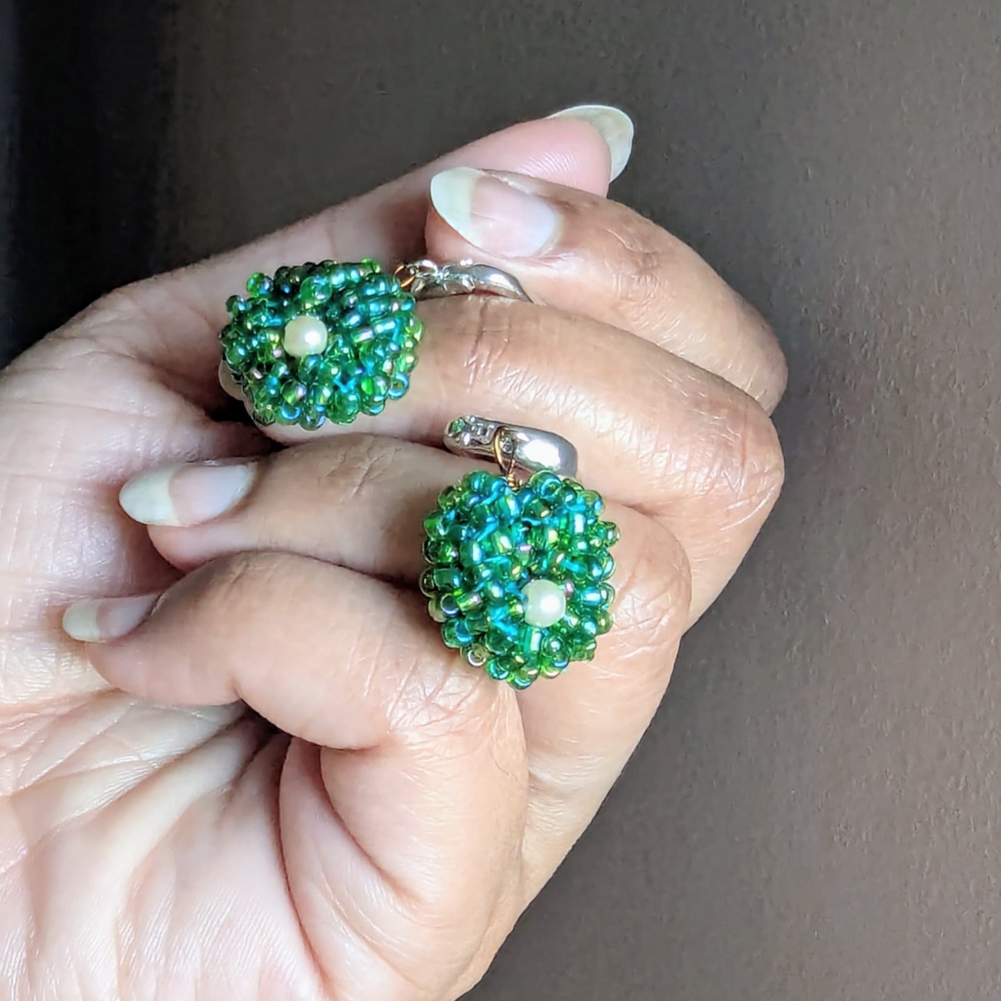 Hand holding Vasanti earrings showing luminous green beads and pearl centres in the Masi Everyday Edit style.