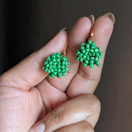 Hand holding a pair of light green handmade seed bead earrings crafted by Mayaani Jewellery UK.