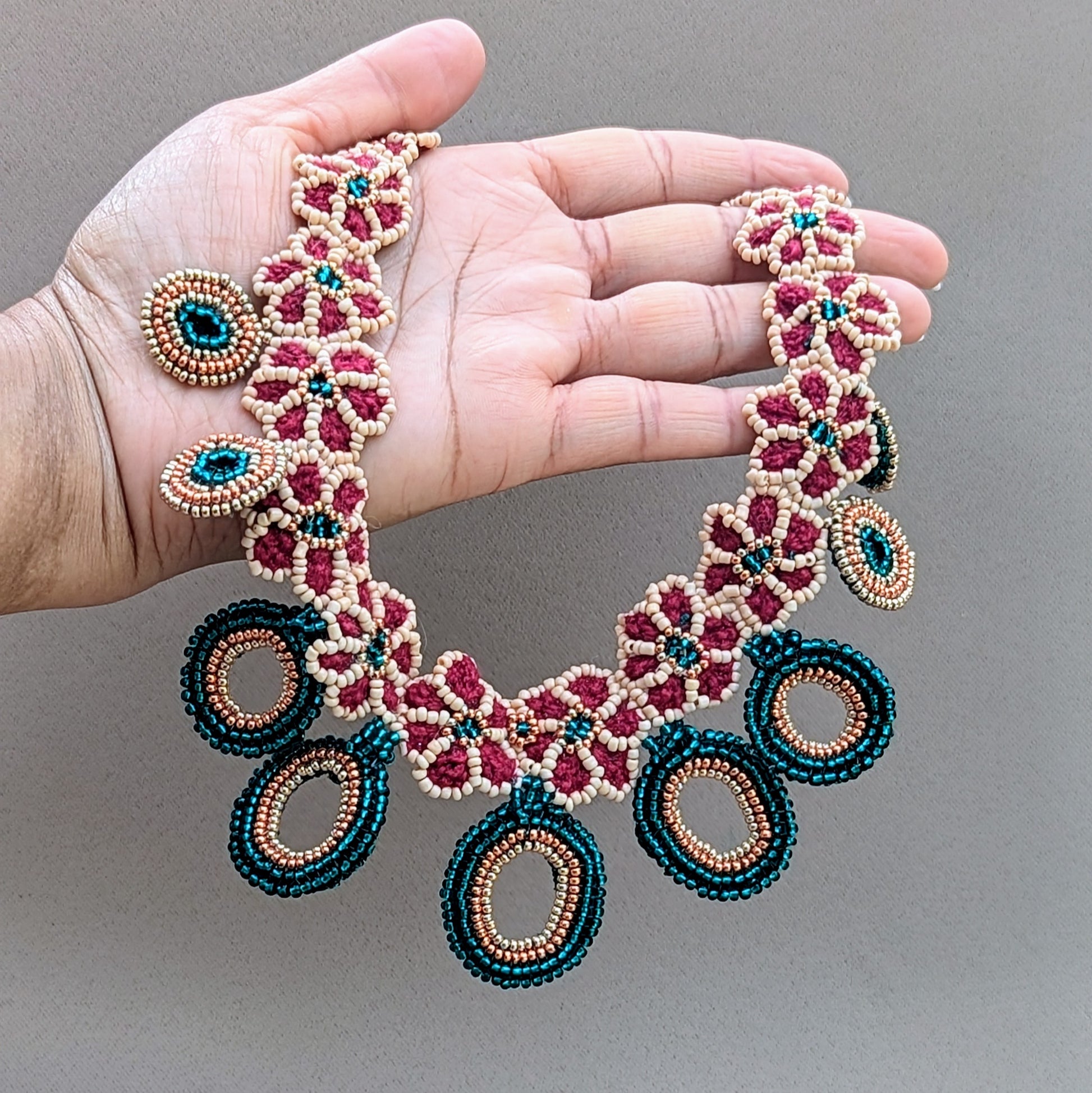 Hand holding a one-of-a-kind statement bridal necklace exclusive to Mayaani Jewellery UK handcrafted in emerald green, peach, red and gold tones.