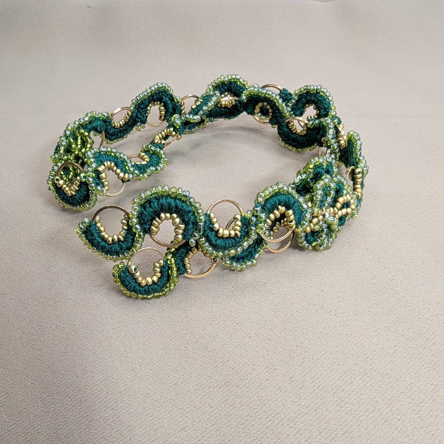 Flat lay of Rukmini handcrafted emerald green and gold statement chain by Mayaani Jewellery UK pictured coiled against neutral backdrop.