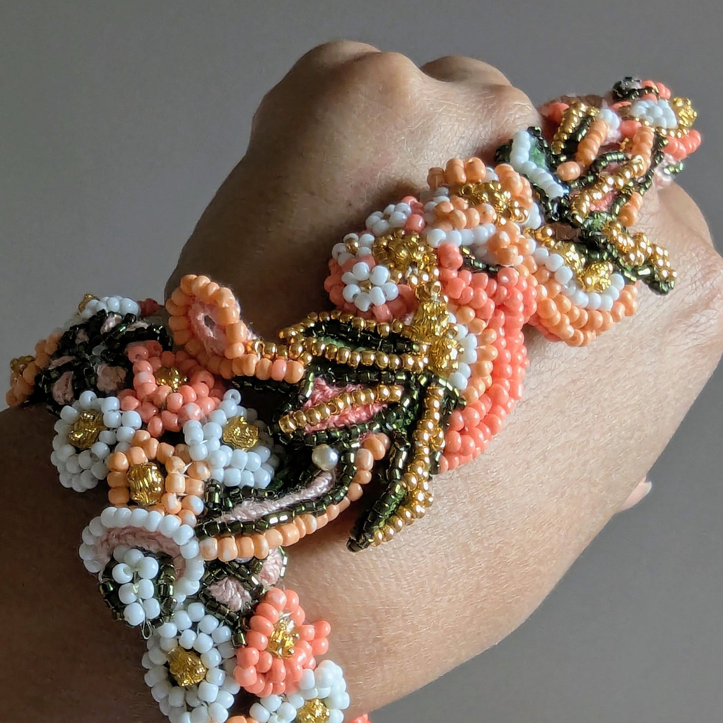 A close up view of the artisan made Padmika 5-in-1 couture Indian wedding occasion haath phool bracelet featuring floral motifs in oranges, greens and white.