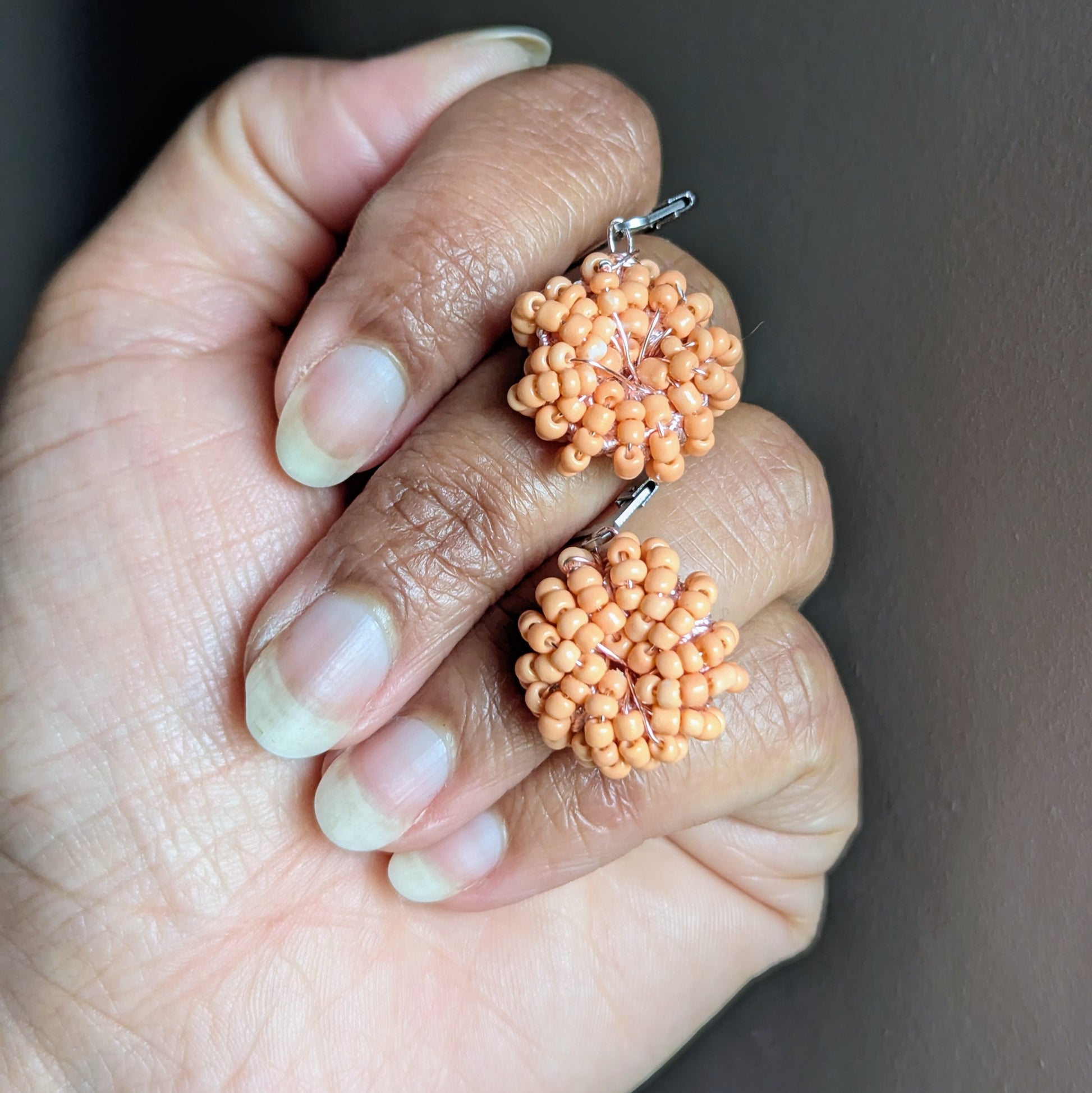 Close-up of delicate peach beaded earrings on neutral background.