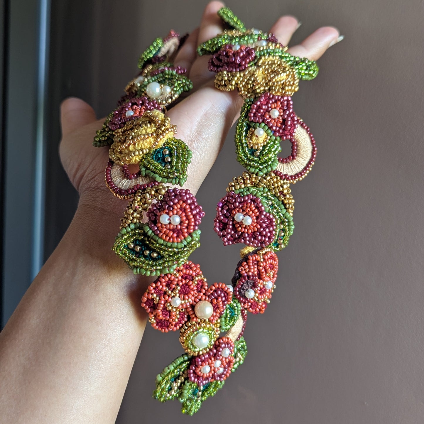 Hand held detailed view of the Rukmini 2-in-1 artisan handmade bead woven necklace designed and handcrafted in the UK for Mayaani Jewellery by Indian artisan Megha. The necklace features luxurious shades and rich textures.