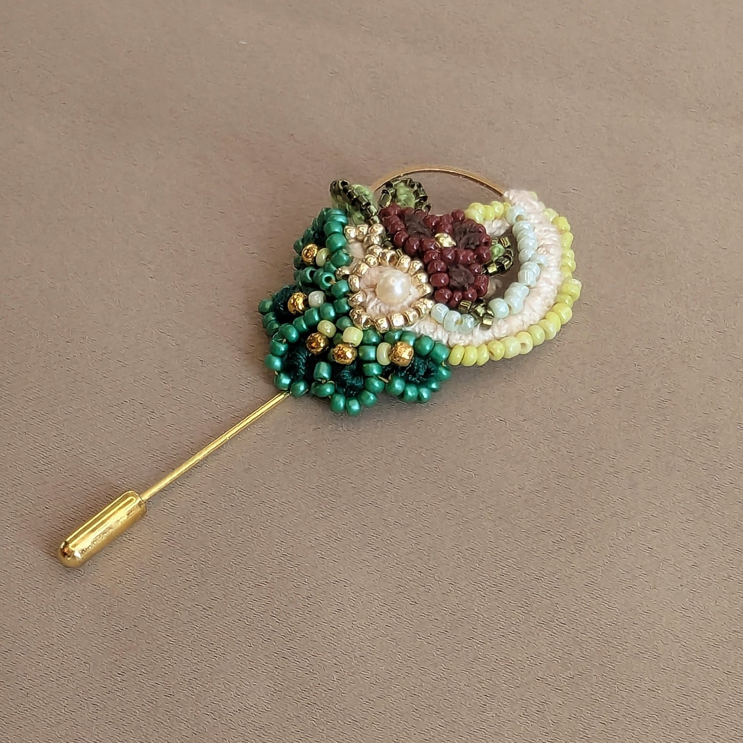 Sarika handcrafted beaded brooch photographed on neutral background featuring emerald green Miyuki beads, coral beadwork, pearl centre and gold stainless steel pin.