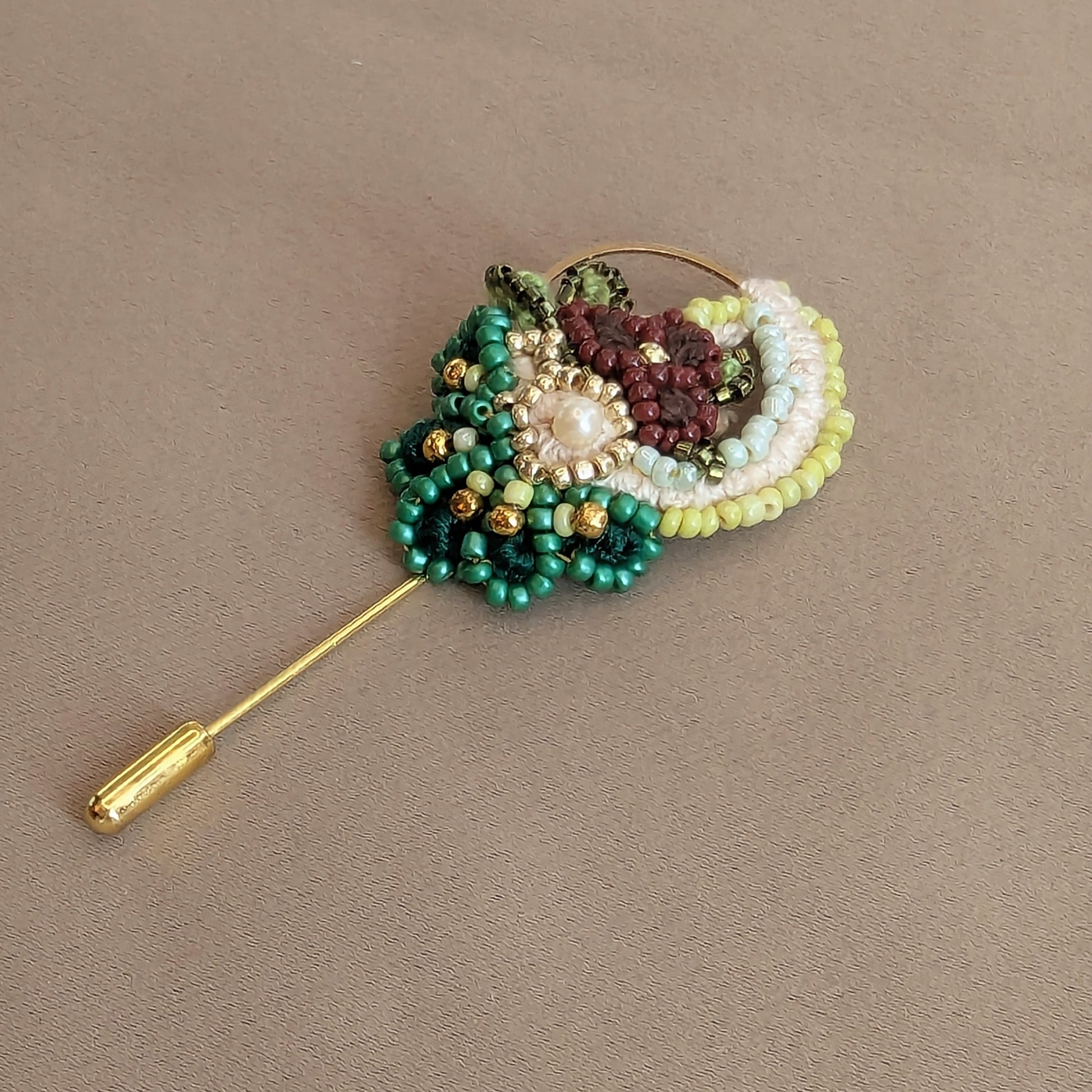Sarika handcrafted beaded brooch photographed on neutral background featuring emerald green Miyuki beads, coral beadwork, pearl centre and gold stainless steel pin.