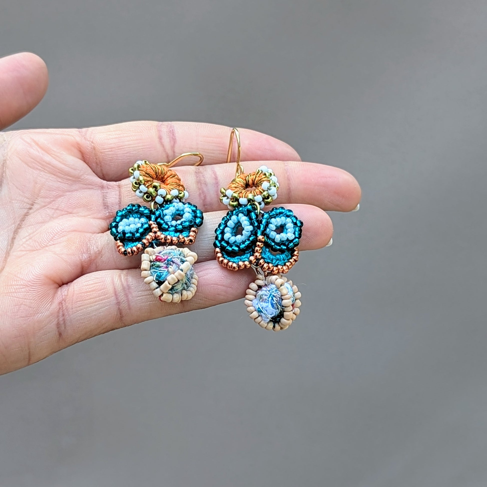 Hand holding a one-of-a-kind blue butterfly earrings with seed bead and crochet detailing, perfect for weddings or special occasions. Ethically handcrafted using vintage upcycled materials by Mayaani Jewellery UK.