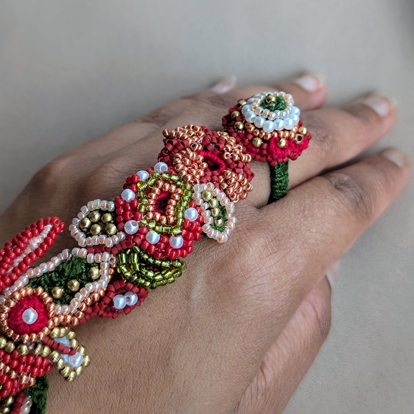 Close up detailed view of the heavily beaded Shreya 5-in-1 Indian hand bracelet  worn on a hand against a neutral backdrop. Made in the UK.