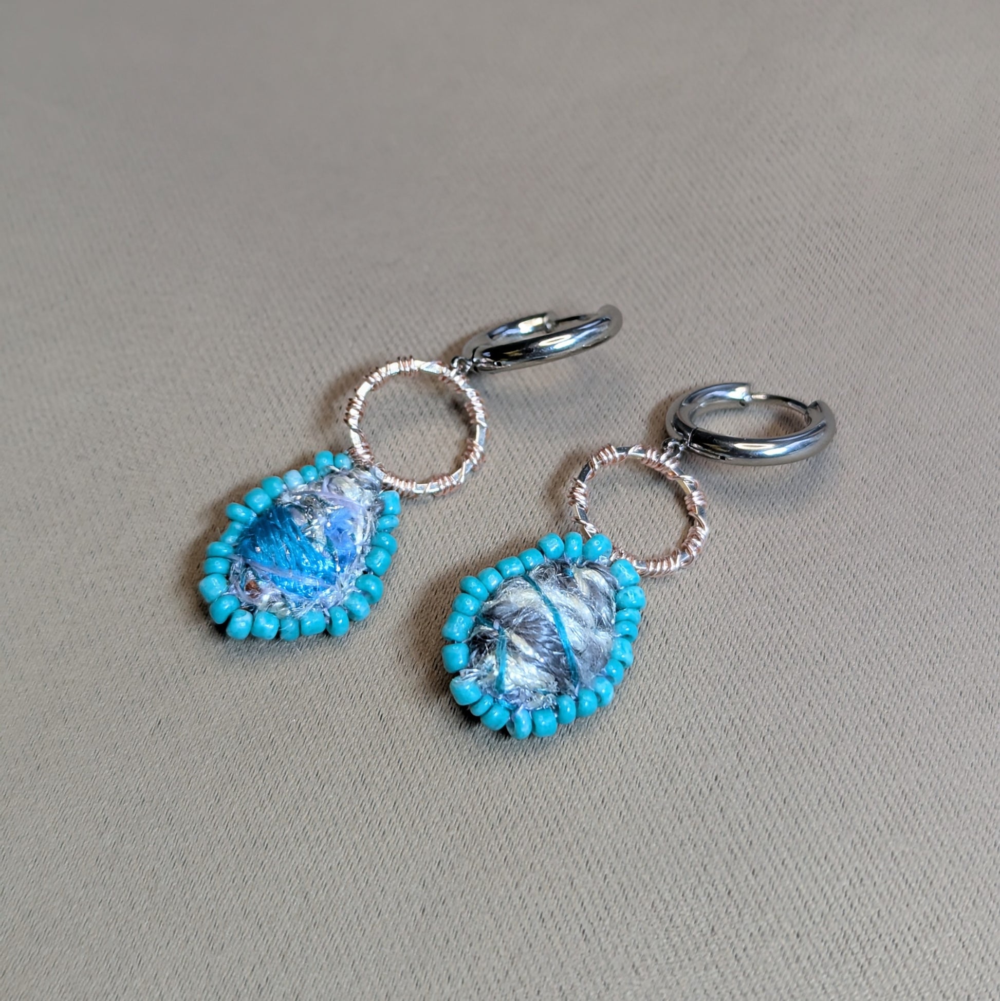 Side view of Tarini asymmetric scrap bead earrings highlighting stainless steel hoops and dimensional textile centres.