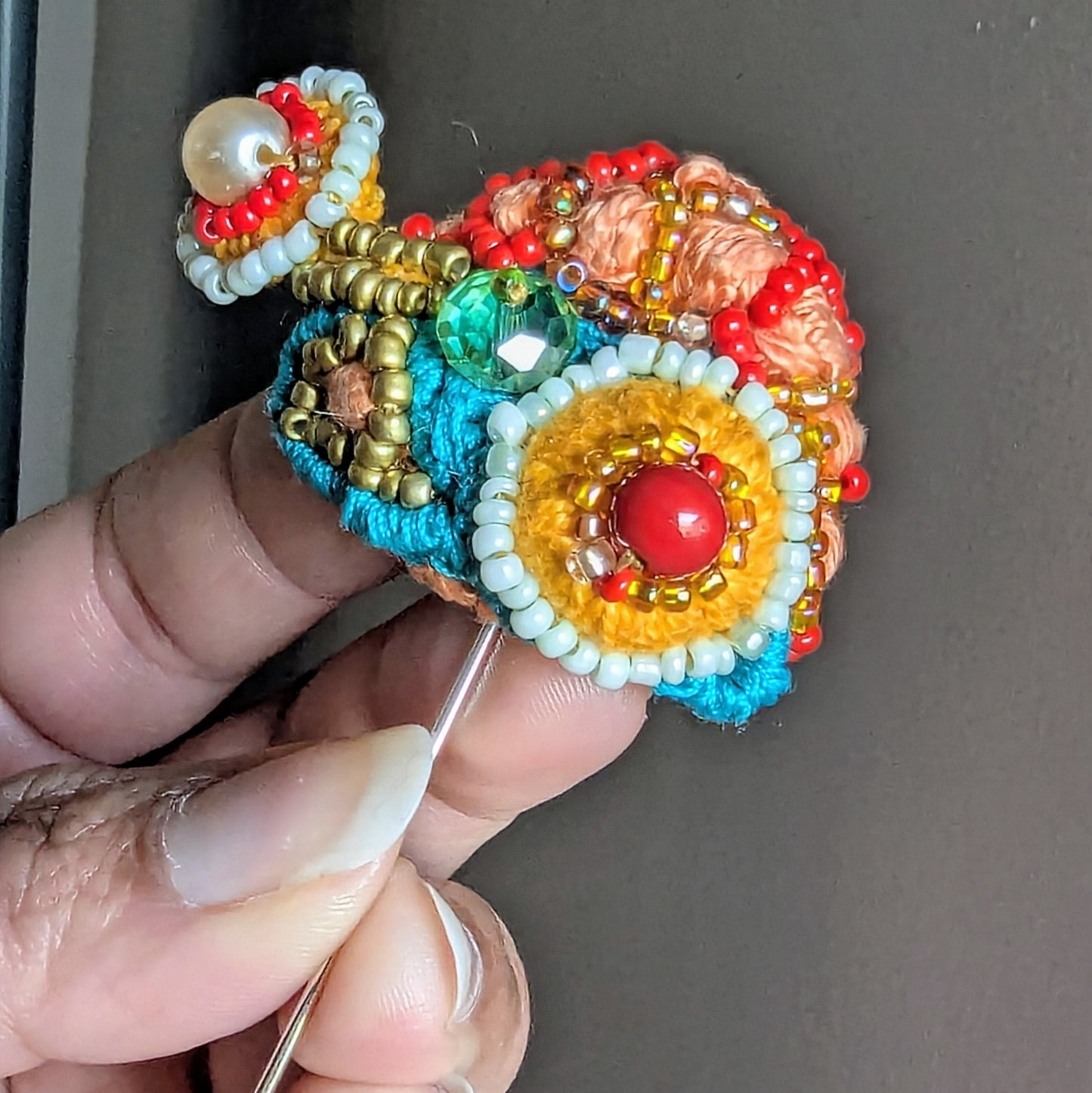 Tejasi one of a kind radiant beaded statement brooch held in hand featuring vintage crystal glass, red and turquoise beads and layered textile embroidery.