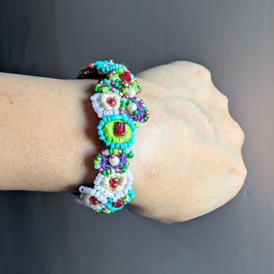 Handcrafted beaded bracelet worn on the wrist, featuring circular crochet motifs with green, turquoise, pearl, and red new and vintage glass seed beads, inspired by a blooming garden and handmade in the UK.