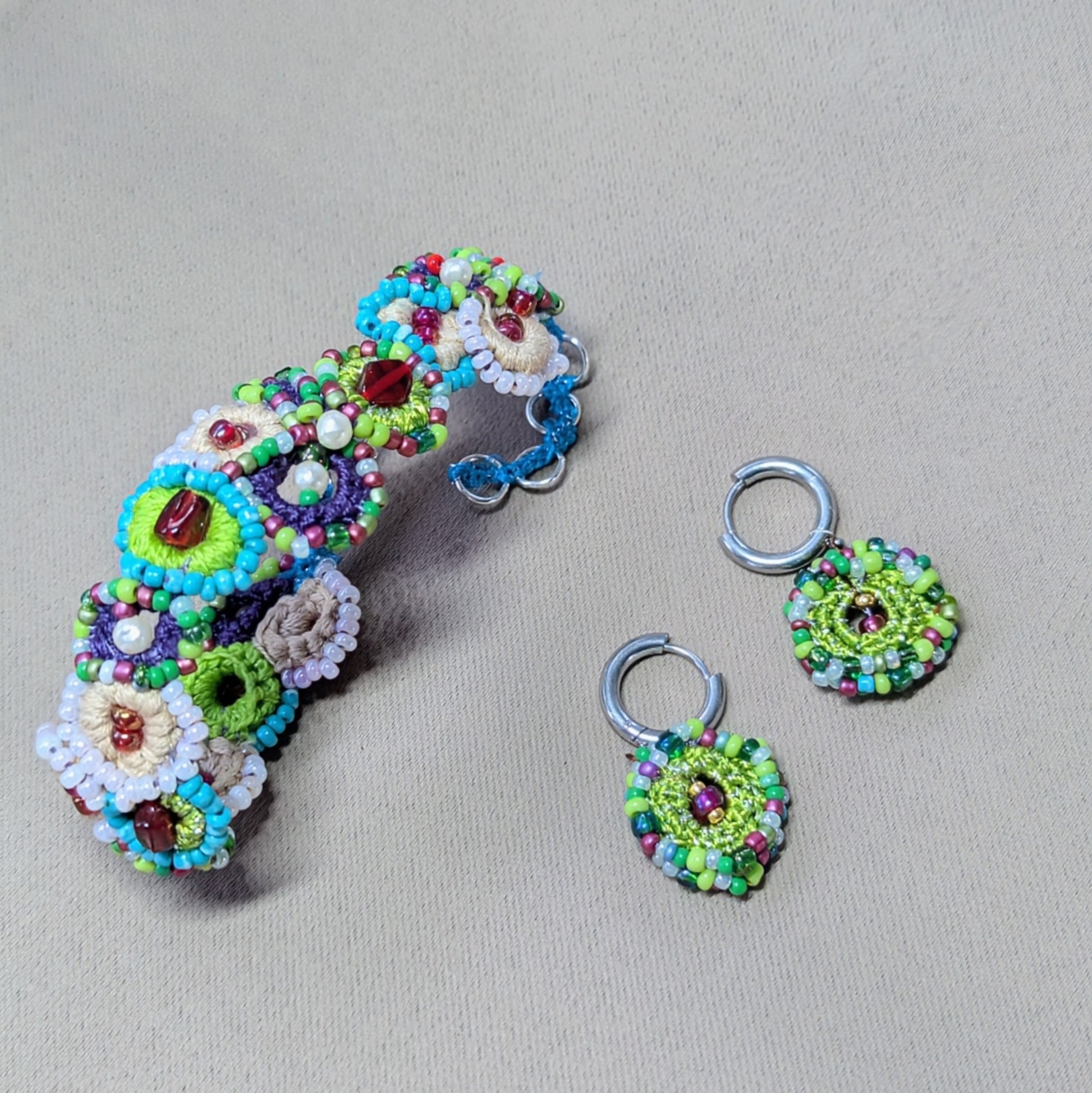 Flat lay of Vana bead crochet earrings with circular floral design, green and blue glass beads, sustainable jewellery.