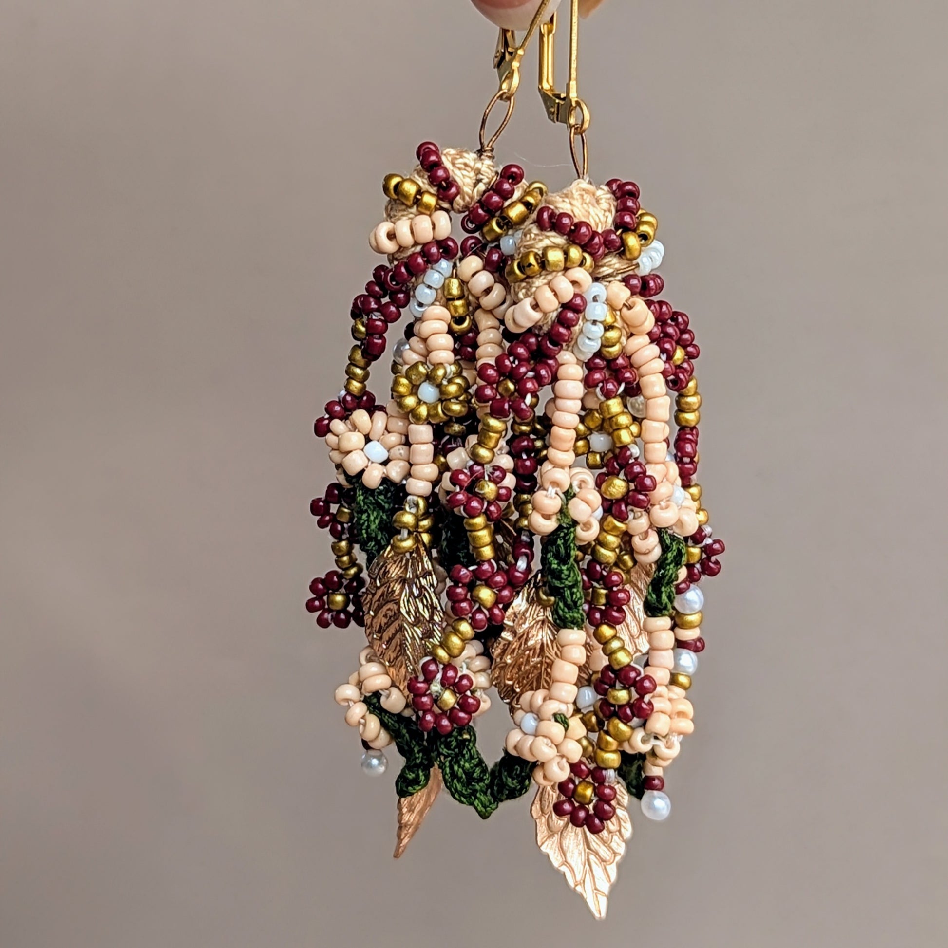 Pair of artisan Indian bridal occasion earrings with intricate beadwork in red, green, gold, and ivory tones, handcrafted by Mayaani Jewellery UK. Features include multiple hand-crocheted strands and gold-plated leaf details.