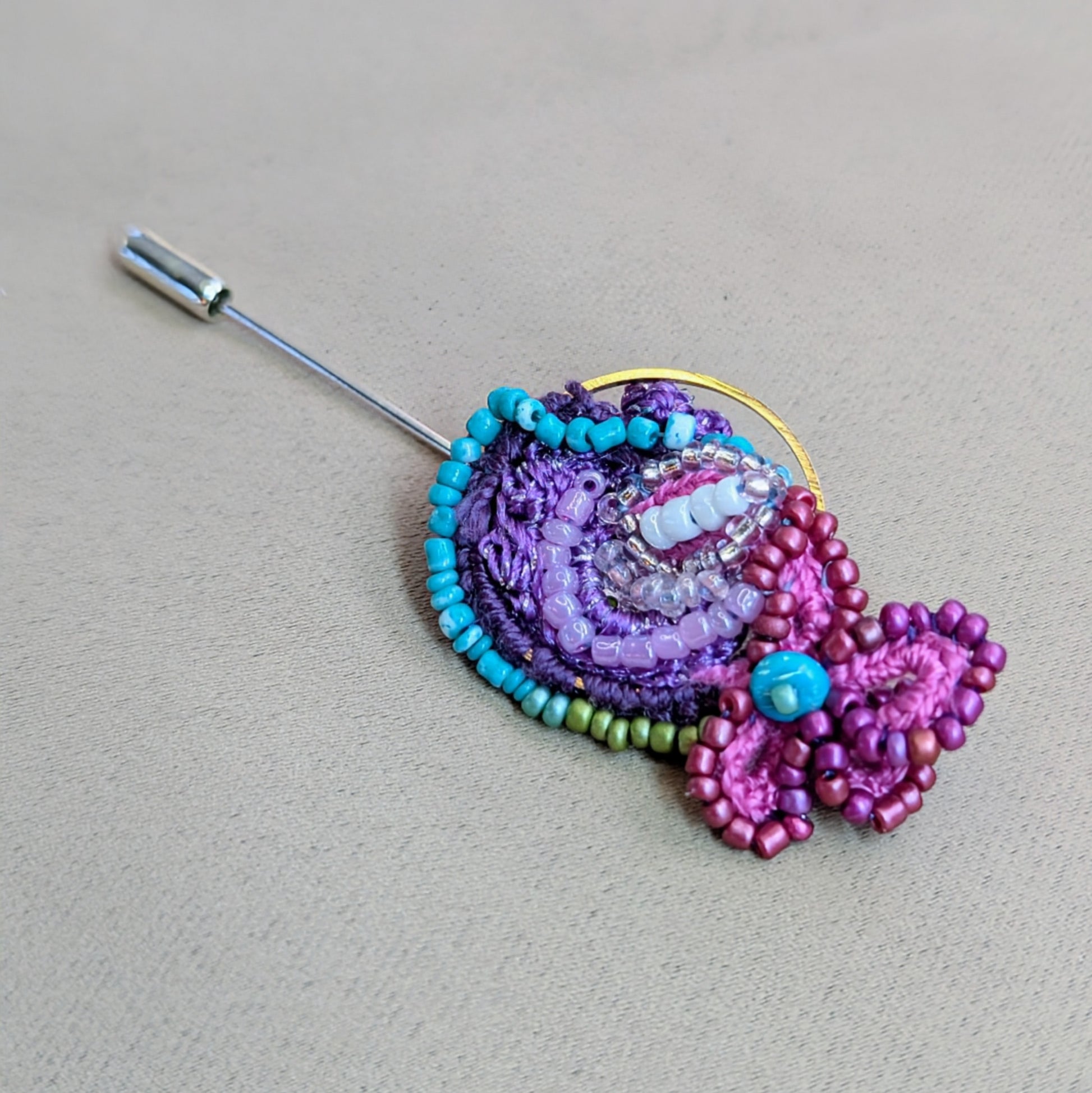 Navira sustainable handmade statement brooch in purple and turquoise tones featuring glass seed bead embroidery, crochet elements and stainless steel pin fastening.