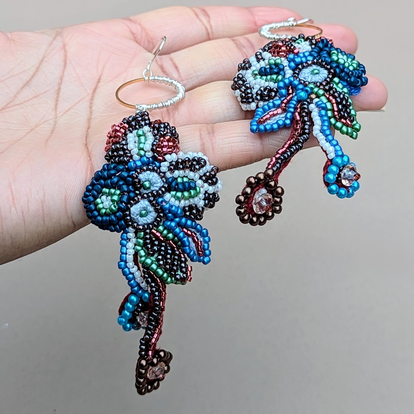 One-of-a-kind Neelara gold ring, red, blue, green, soft white beaded earrings, held in hand, handcrafted with crochet, wire wrapping and bead embroidery.