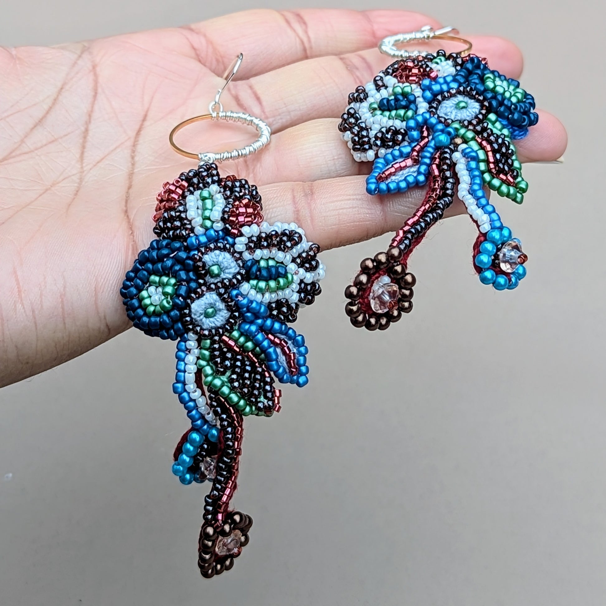 One-of-a-kind Neelara gold ring, red, blue, green, soft white beaded earrings, held in hand, handcrafted with crochet, wire wrapping and bead embroidery.