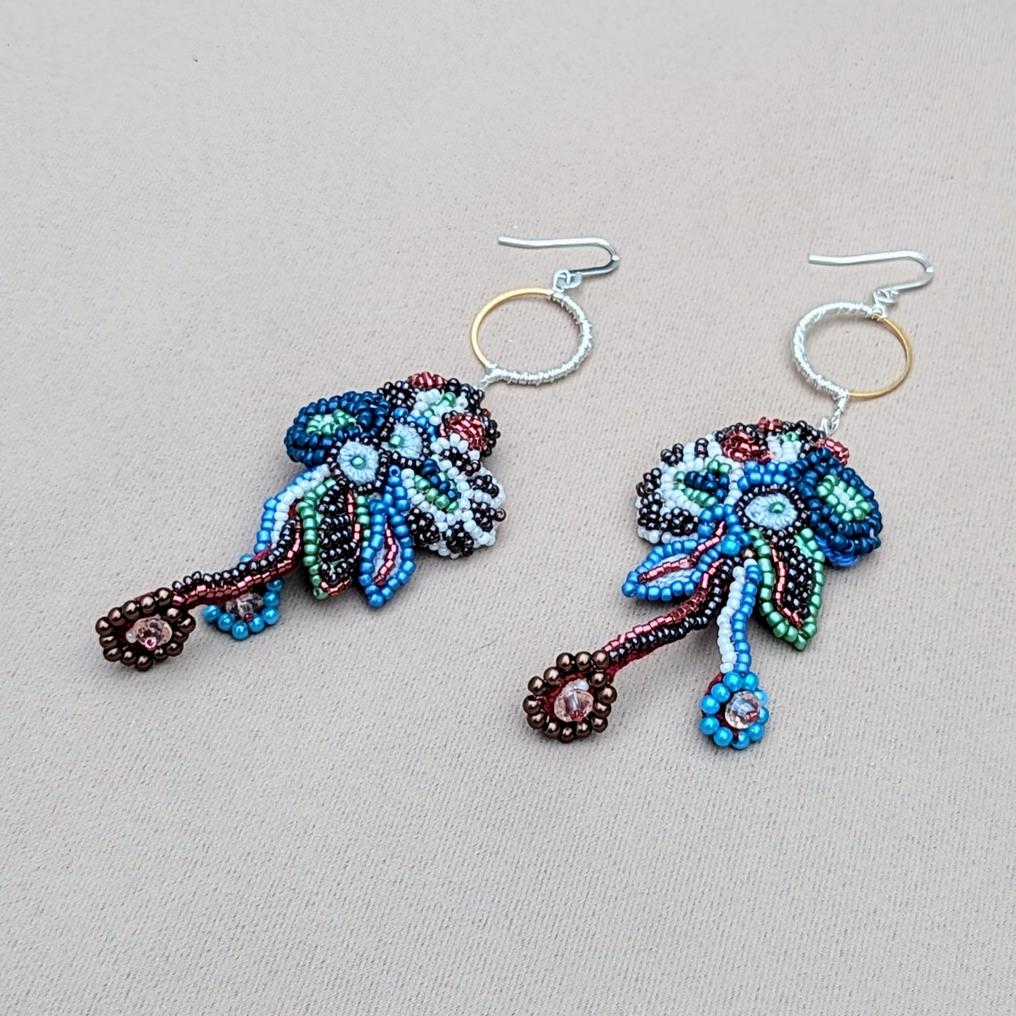 Side profile view of an abstract pair of handmade Indian statement earrings in red blue soft white and gold with flowing bead embroidery details.