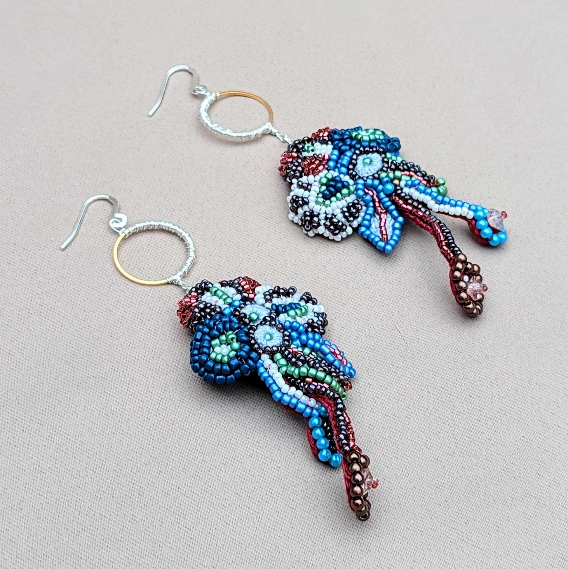 Close up view of artisan beaded earrings inspired by movement and sea-like forms, featuring gold hoops and intricate beadwork.