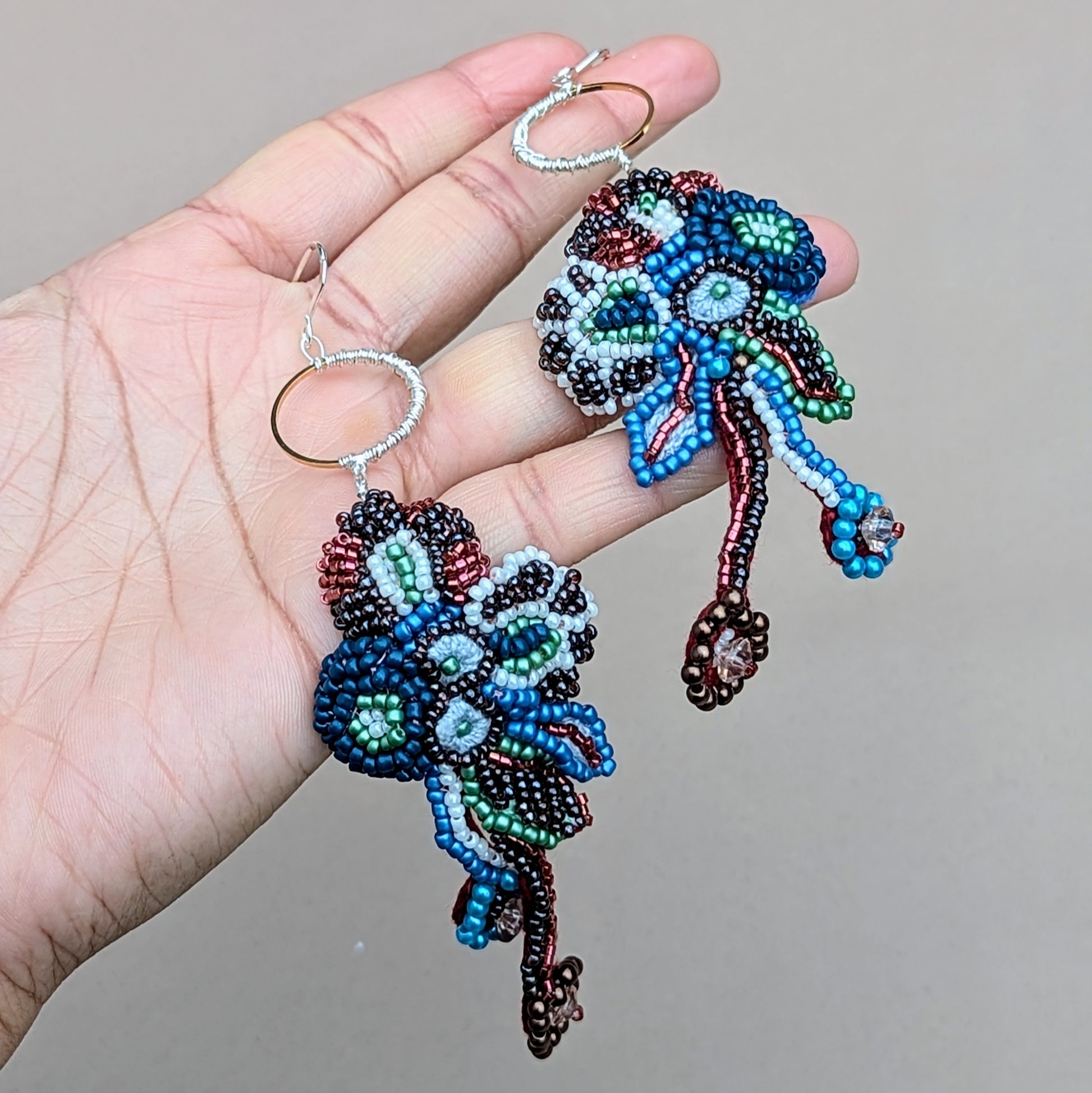Neelara abstract beaded earrings shown in hand, highlighting flowing textures and mixed bead embroidery.