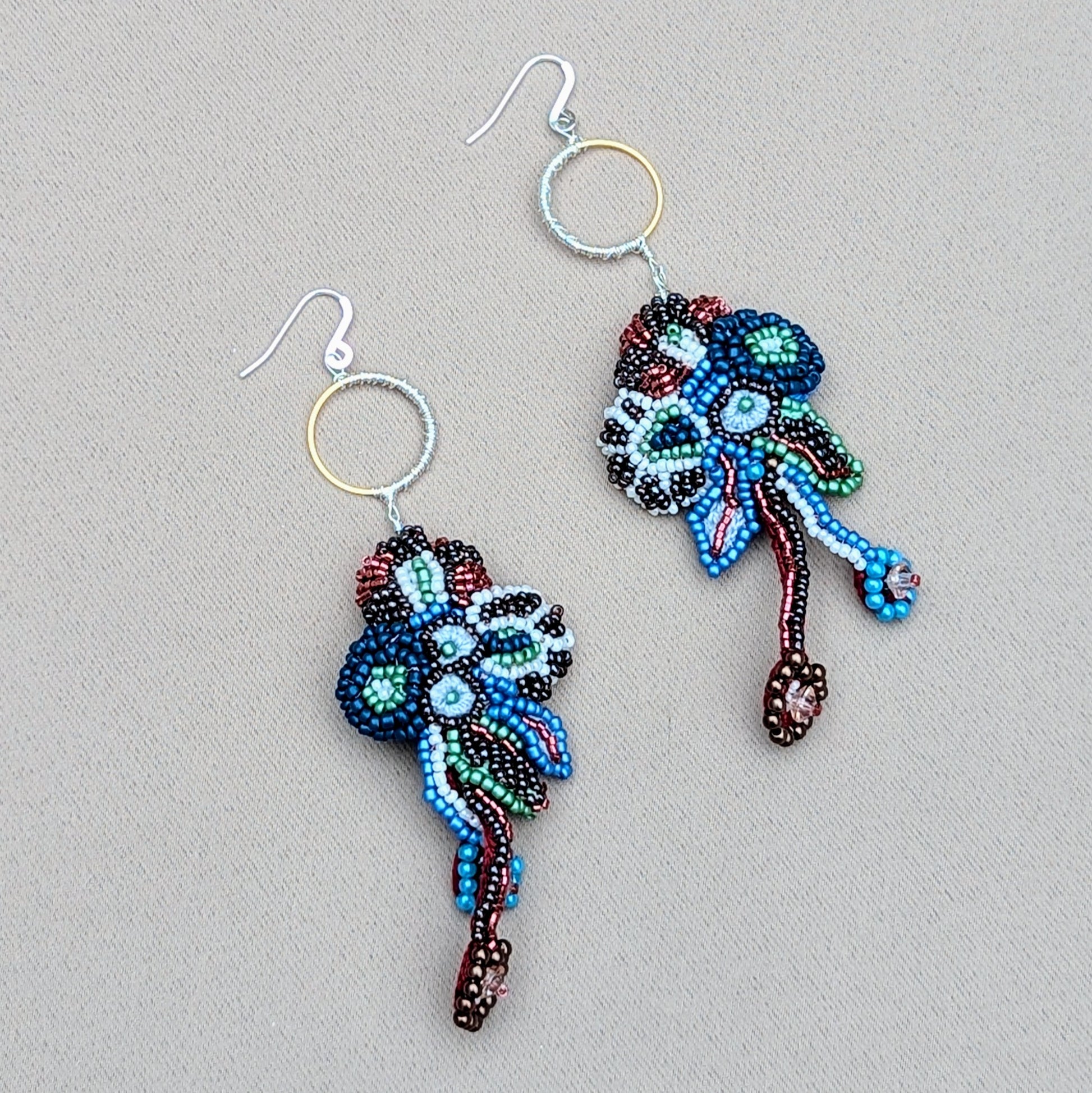 Abstract Neelara beaded statement earrings with red, blue and gold tones, artisan-crafted in the UK using glass seed beads, gold stainless steel hoops and sustainable jewellery techniques.