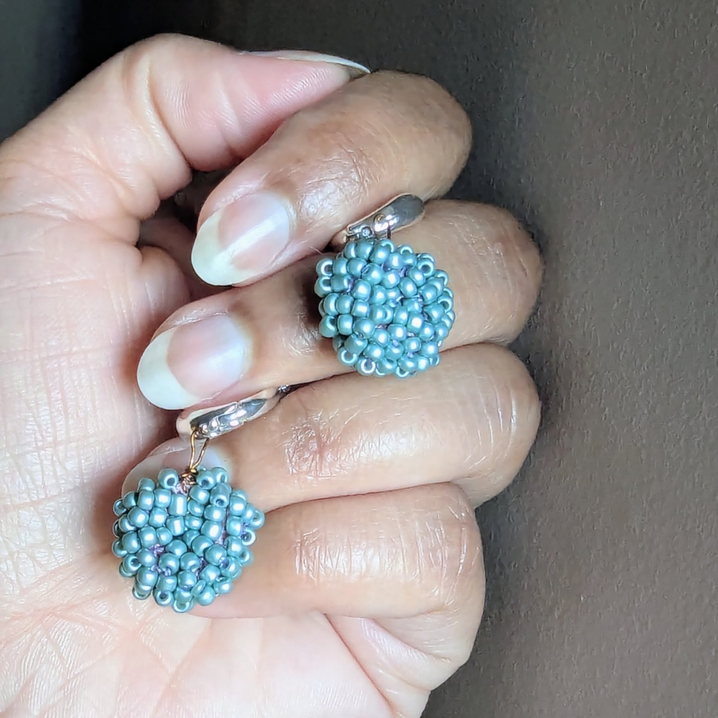 Hand holding Masi Nila earrings showing intricate blue beadwork and antique bronze wire craftsmanship.