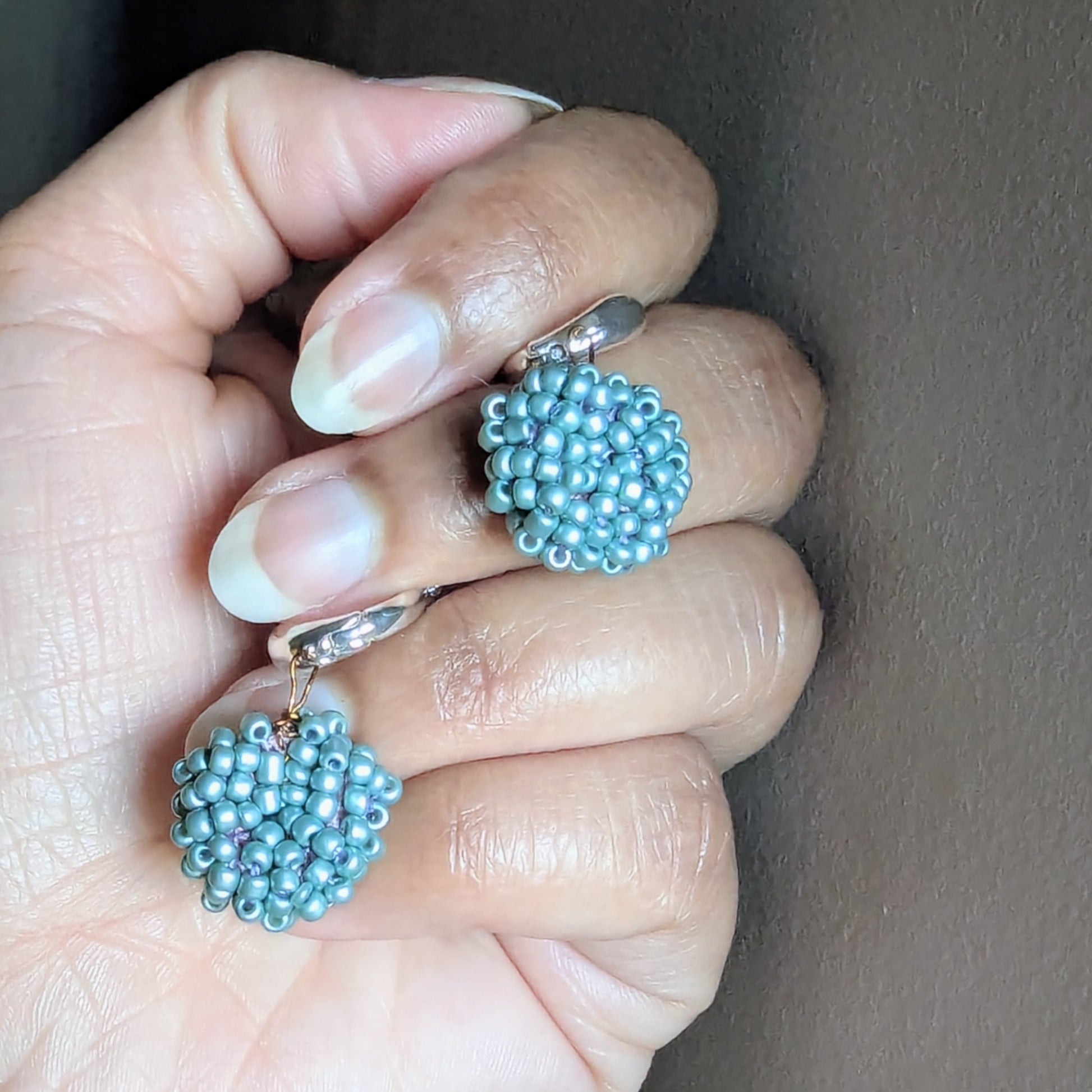 Hand holding Masi Nila earrings showing intricate blue beadwork and antique bronze wire craftsmanship.