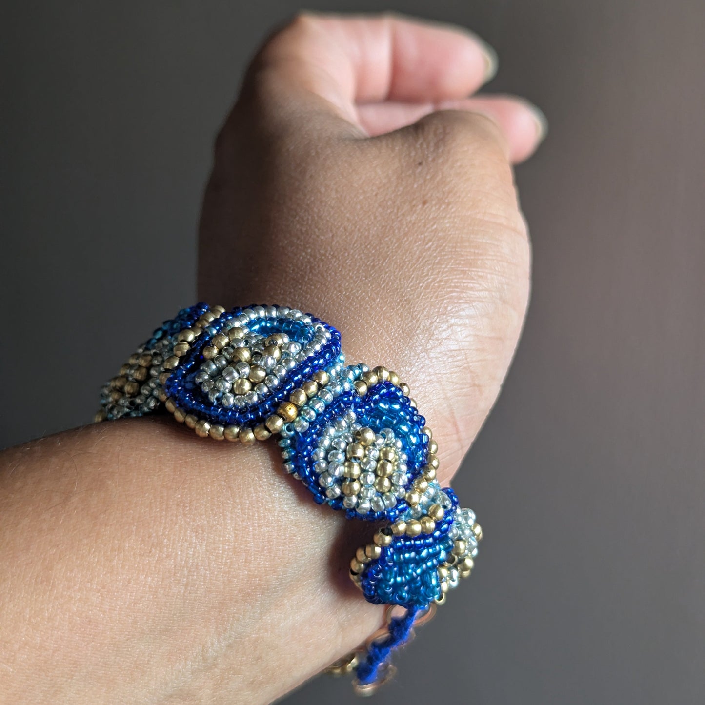 Nira bracelet close up on wrist - cobalt teal and gold Miyuki seed beads with rose gold brass flower detail.
