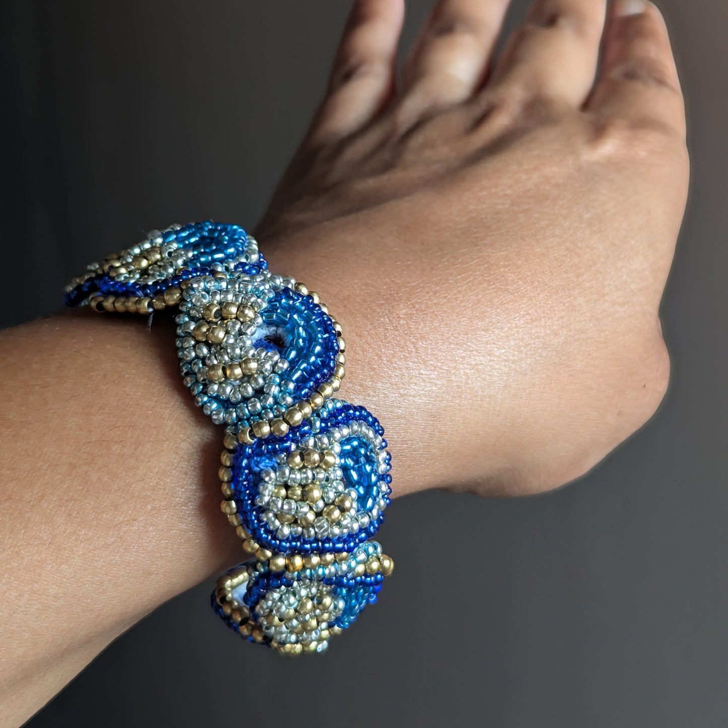 A close up of a hand wearing Nira bracelet on wrist - cobalt blue and gold beadwork texture detail.