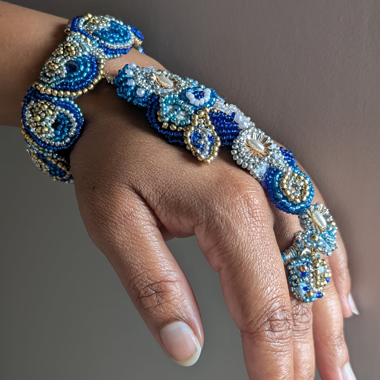 Nira 5-in-1 bracelet side view on wrist - cobalt blue and gold beadwork texture detail.