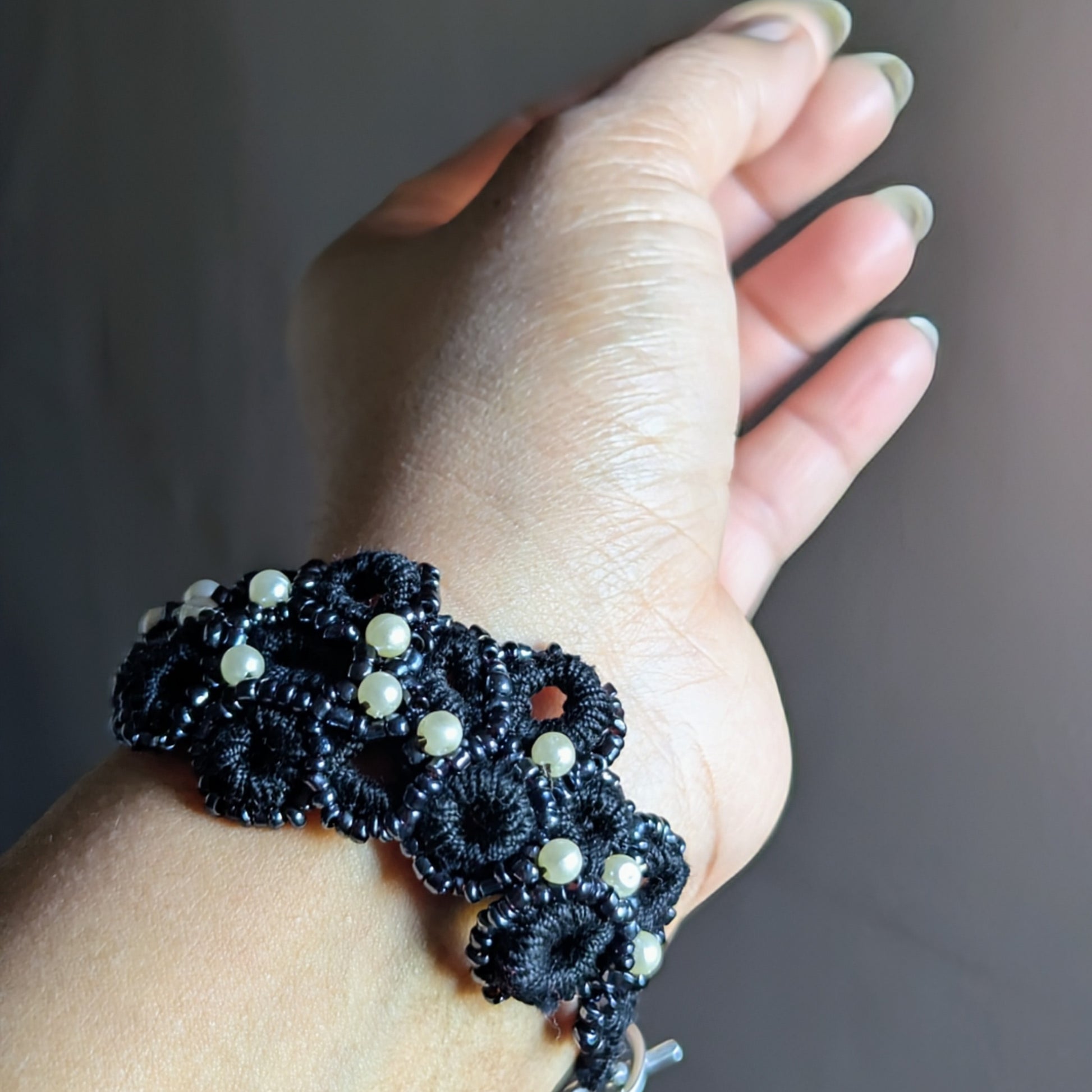 Side view of one-of-a-kind black pearl-accent bracelet with stainless steel clasp photographed on a wrist.