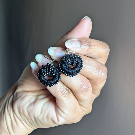 Hand holding a pair of black bead-crochet earrings with vintage pearls and stainless steel hooks.