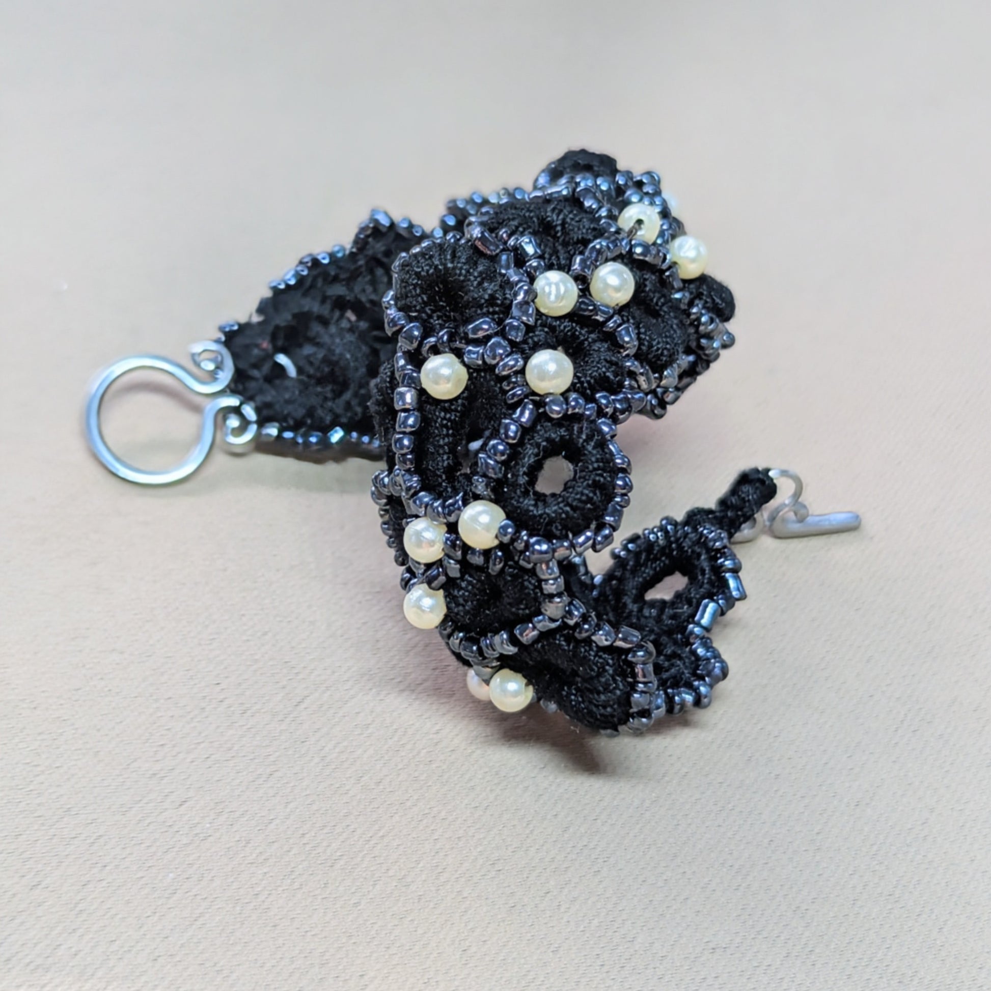 Sustainably crafted black statement bracelet with vintage pearls photographed on neutral fabric.