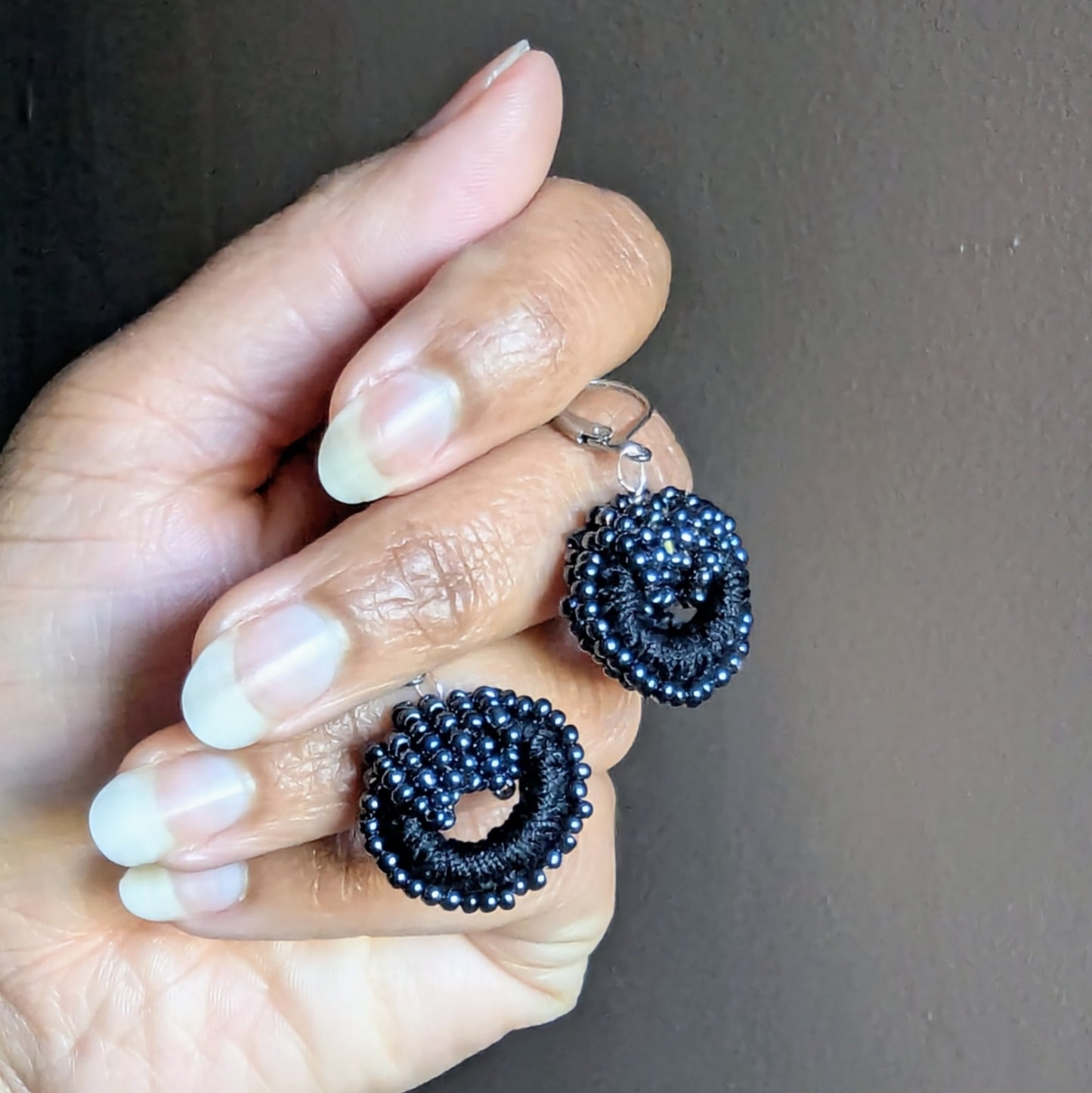 Artisan-made black crochet and bead earrings shown held against a soft grey background.