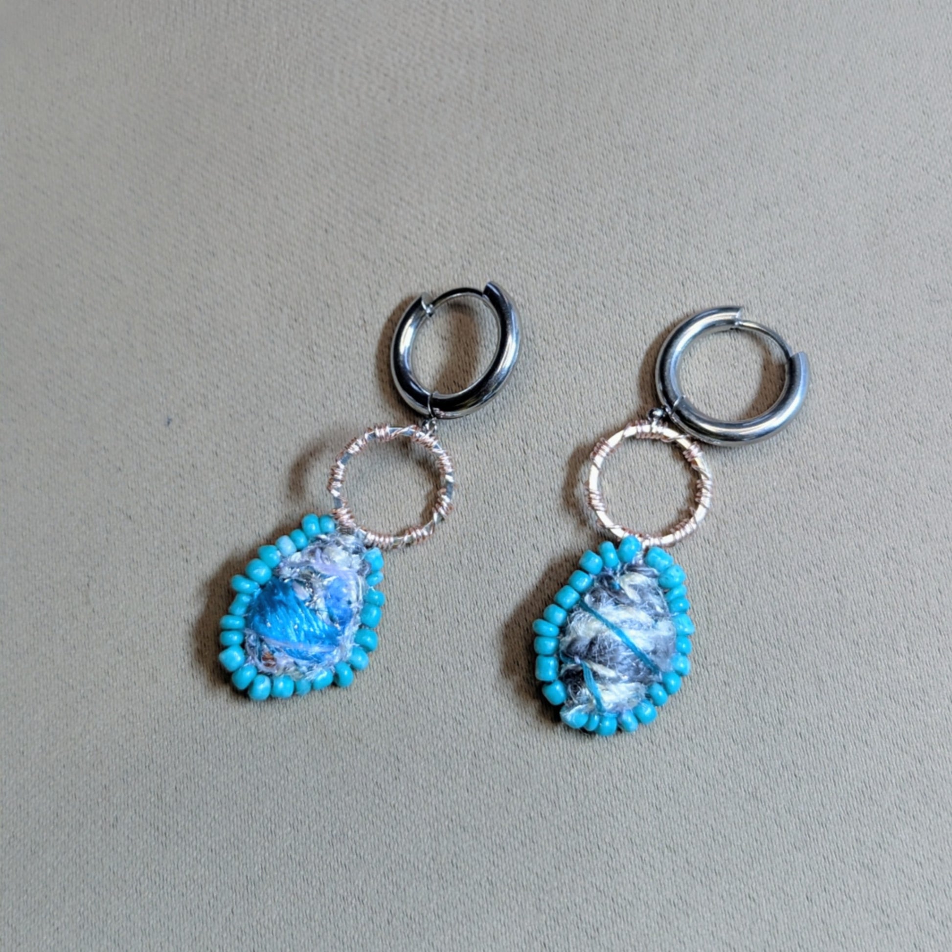 Tarini asymmetric scrap bead earrings on neutral fabric background, vintage turquoise  glass seed beads and textile art centres.