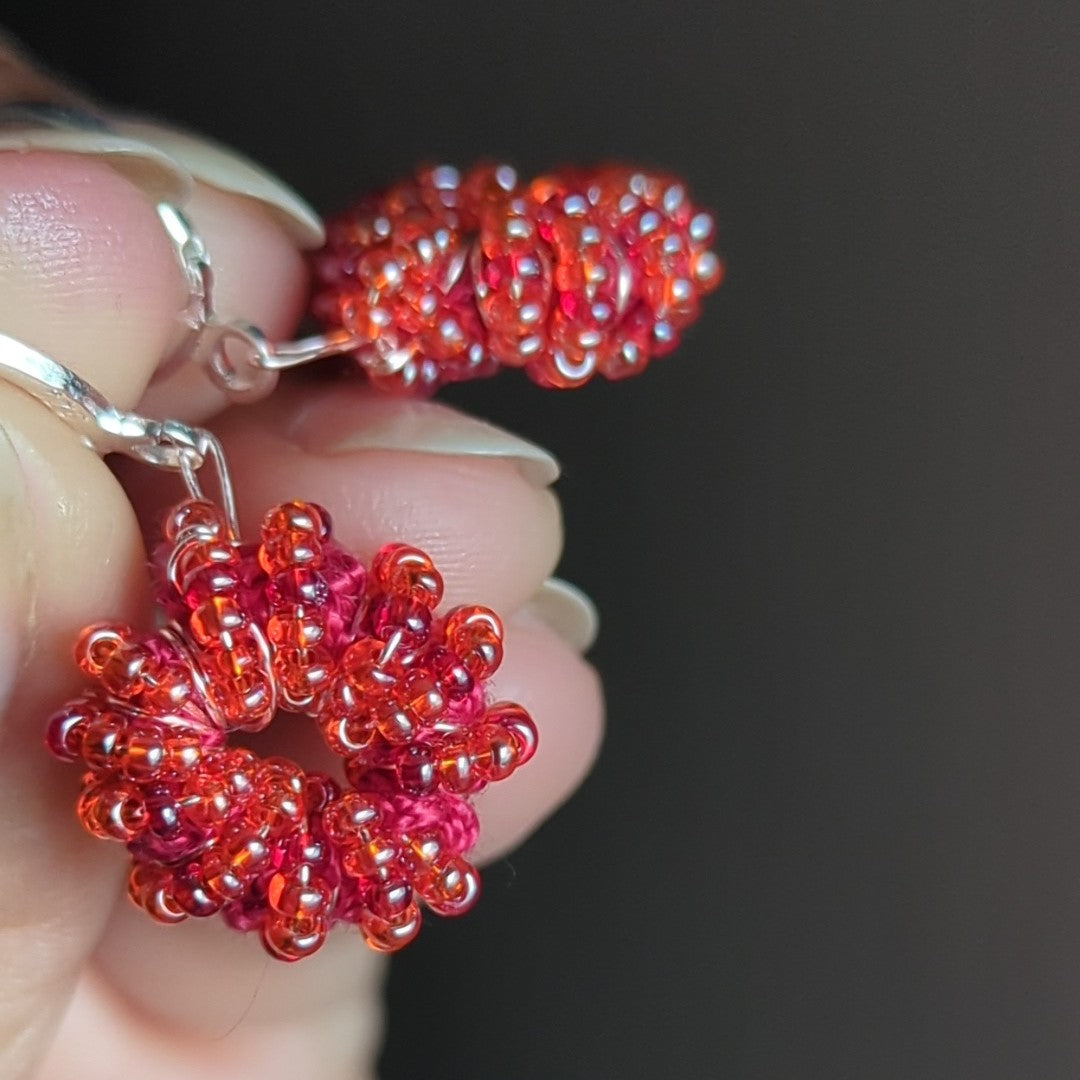 Hand-held image of bold orange-red earrings catching natural light.