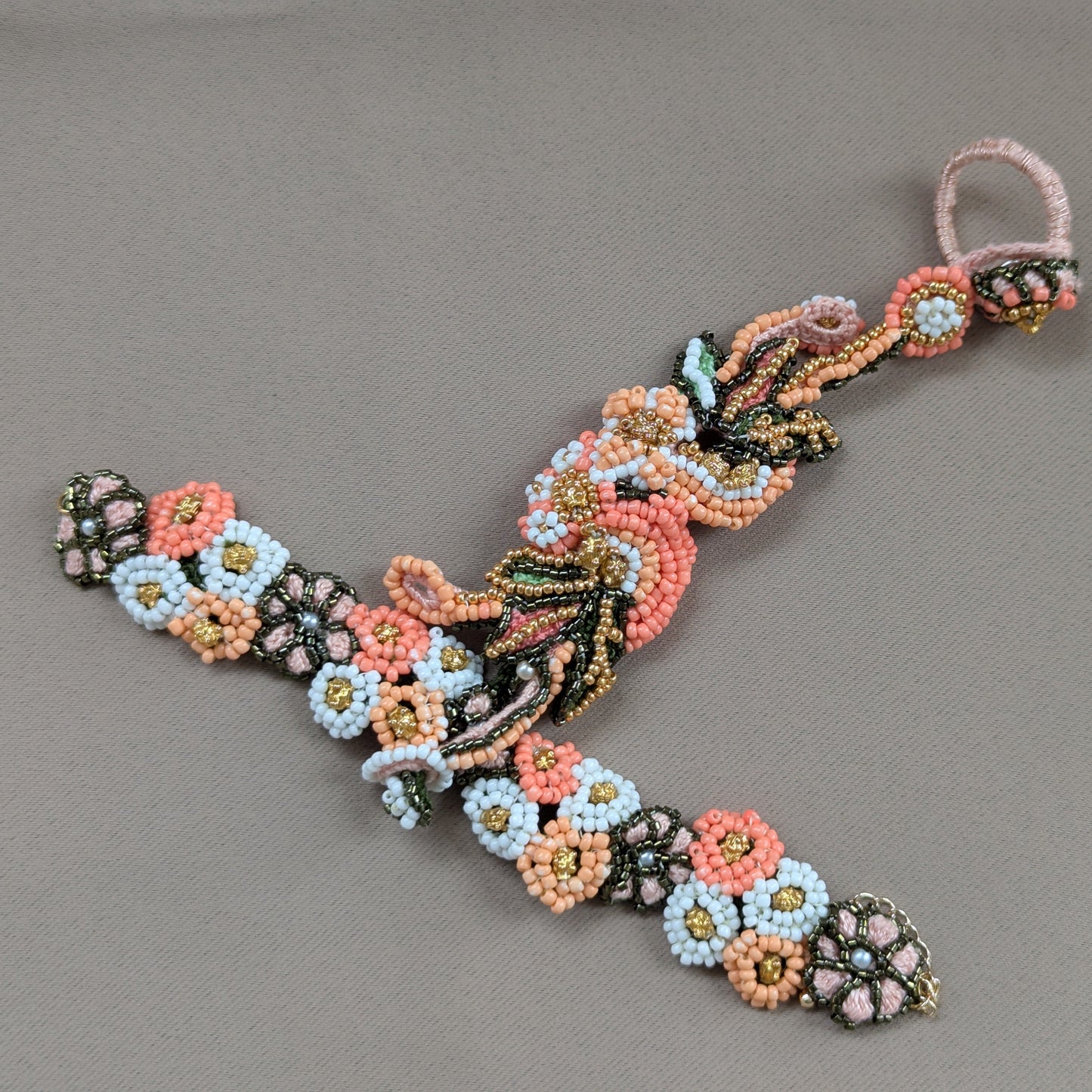 Close up view of the Padmika 5-in-1 intricately hand beaded peach, green, white and gold Indian hand bracelet made in the UK.