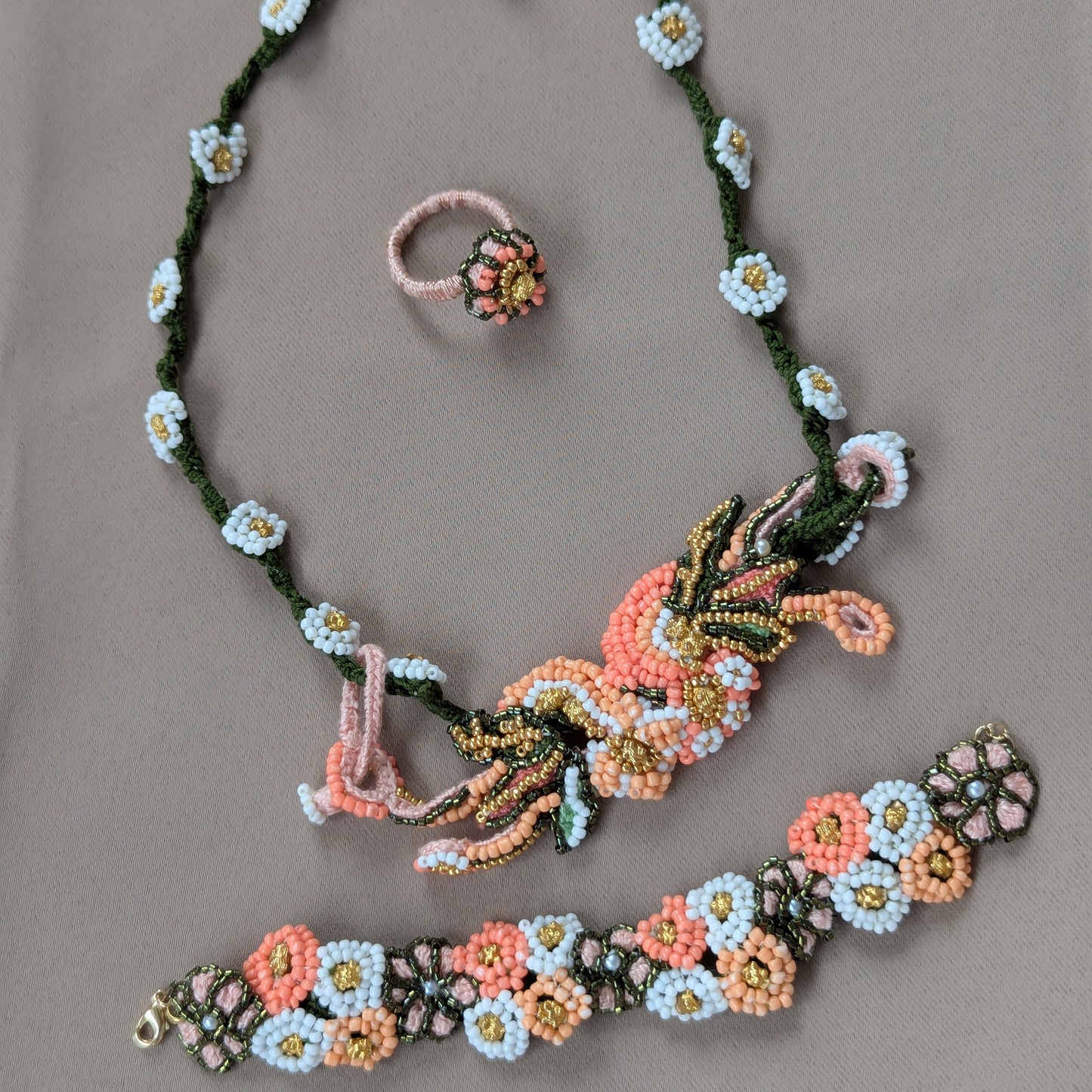 View from above of the Padmika 5-in-1 heavily beaded peach, green and gold wrist bracelet, ring and necklace against a grey backdrop.