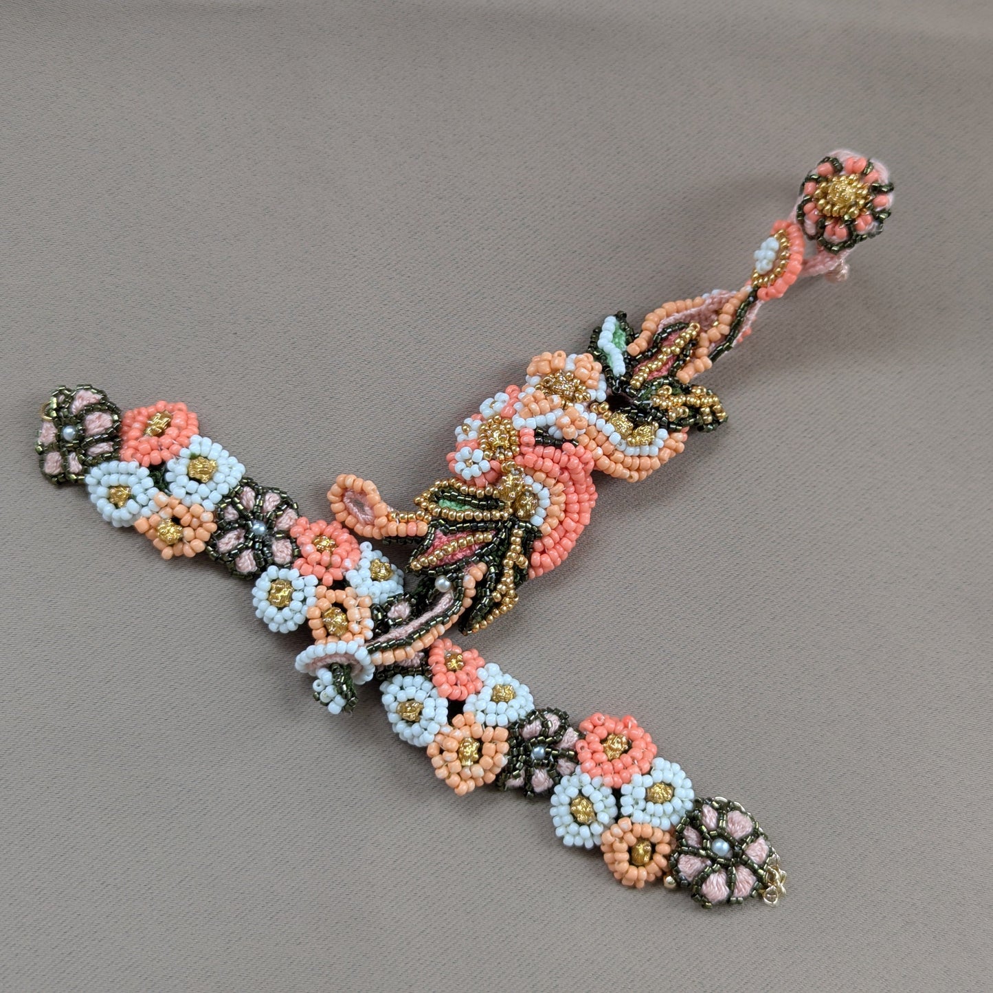 Flat lay view of the Padmika 5-in-1 Indian haath phool bracelet featuring botanical floral motifs in rich hues of peach, orange, green and white in a mixture of seed beads including vintage gold beads.