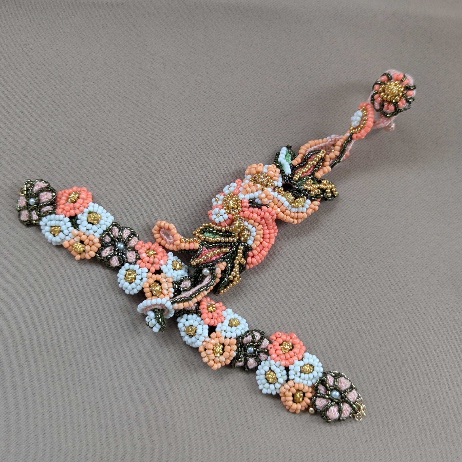 Flat lay view of the Padmika 5-in-1 Indian haath phool bracelet featuring botanical floral motifs in rich hues of peach, orange, green and white in a mixture of seed beads including vintage gold beads.